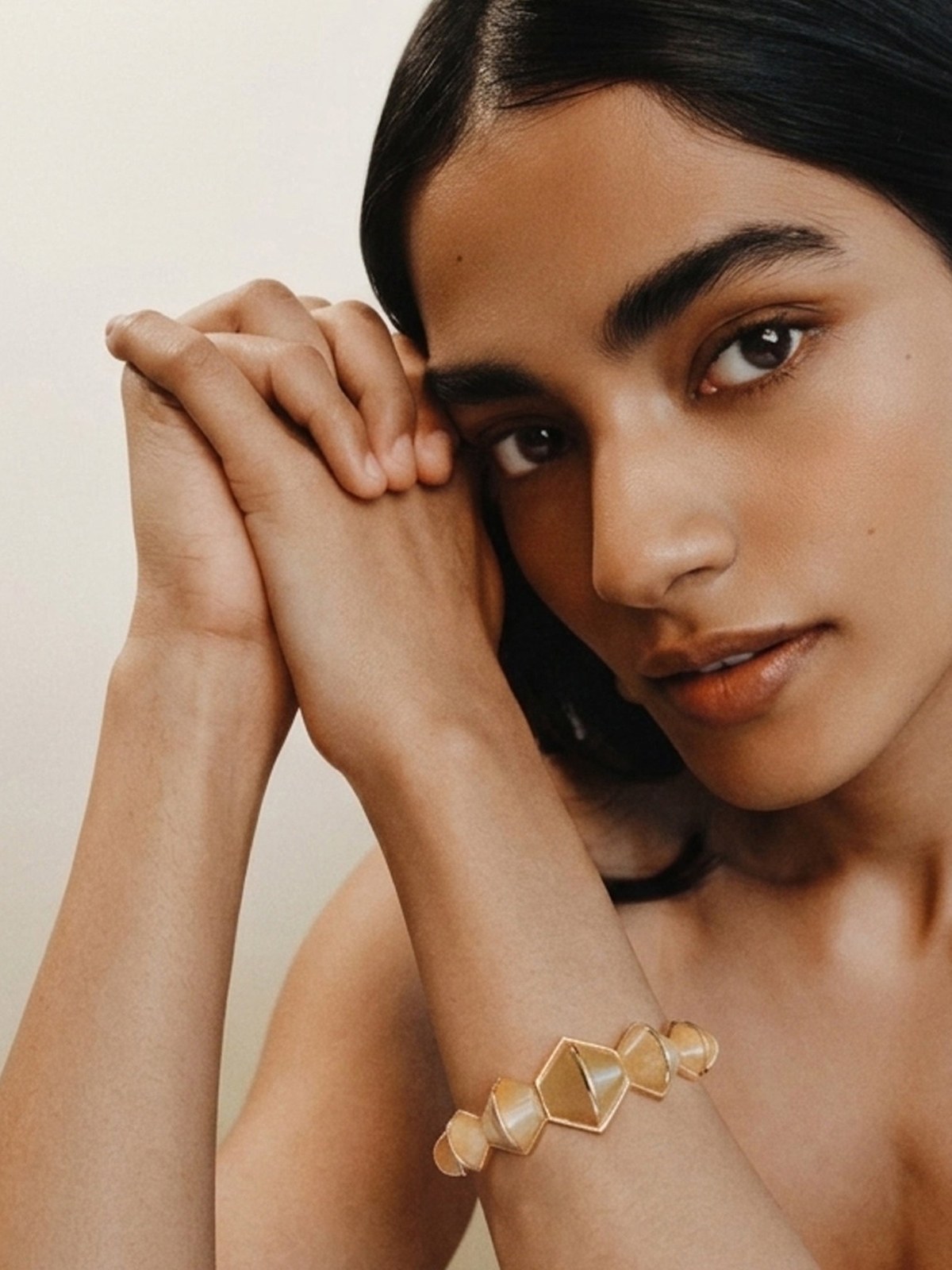 Model wearing a geometric bracelet with her hands beside her face