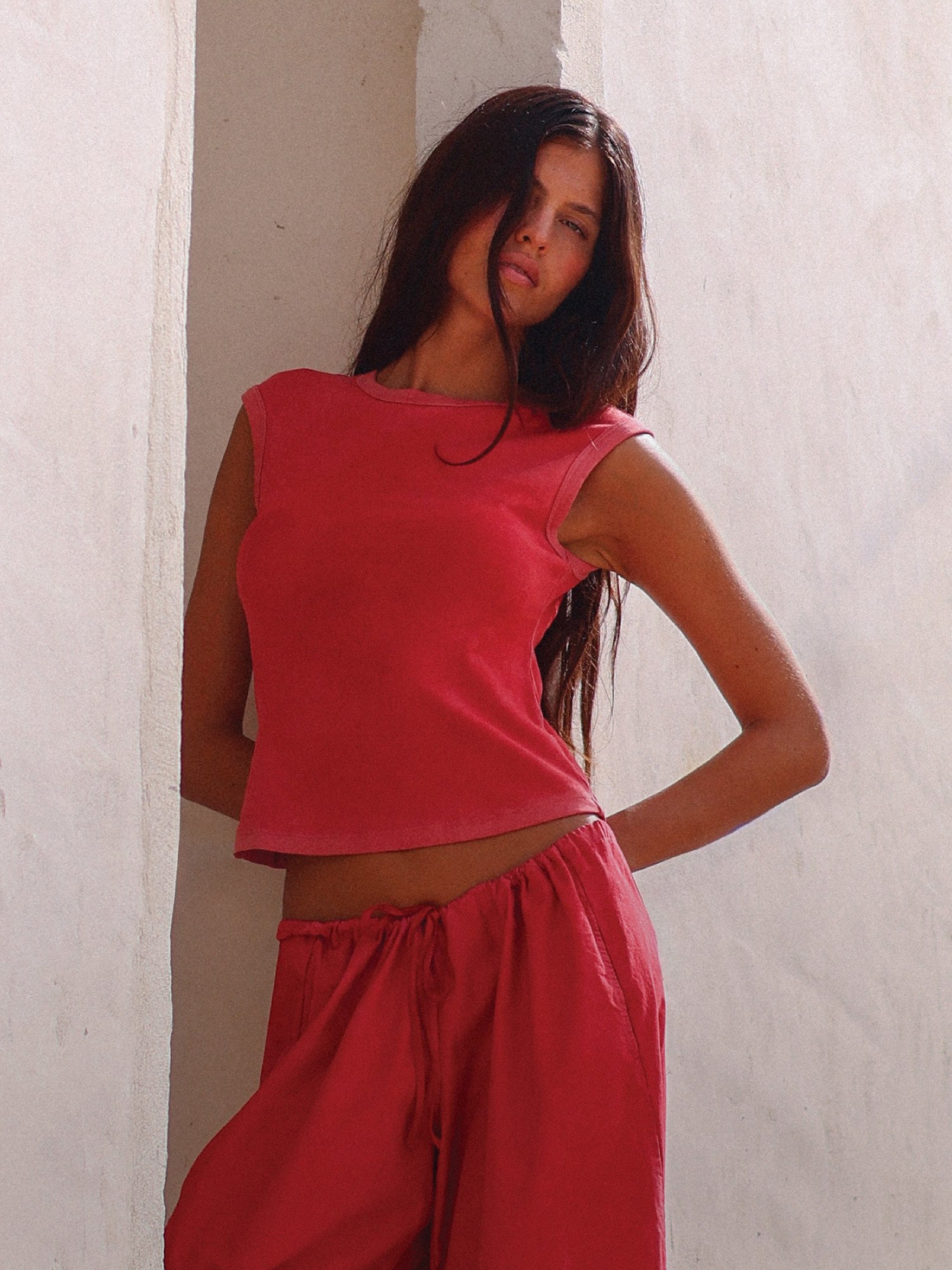 Woman in a coral top and pants leaning in a whitewashed archway