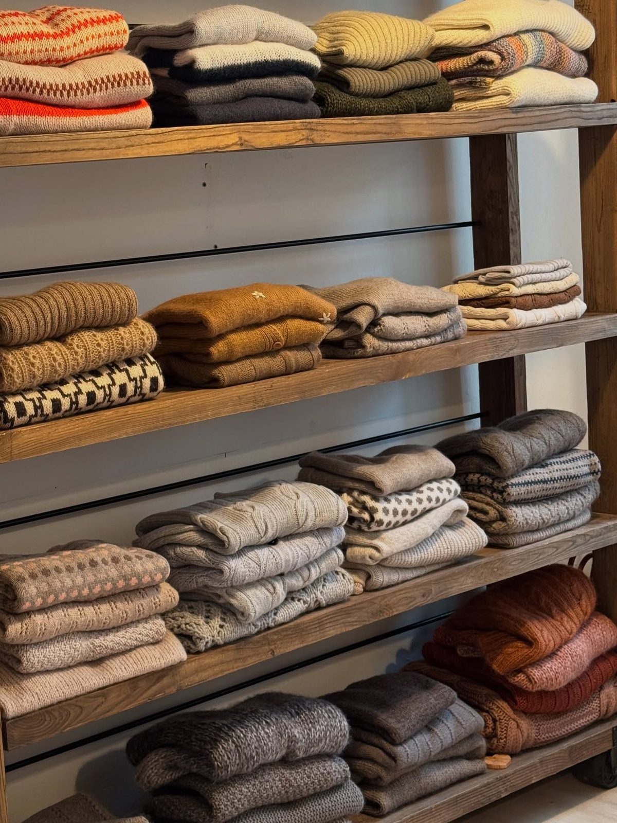 Wooden shelves stacked with knitwear in warm tones
