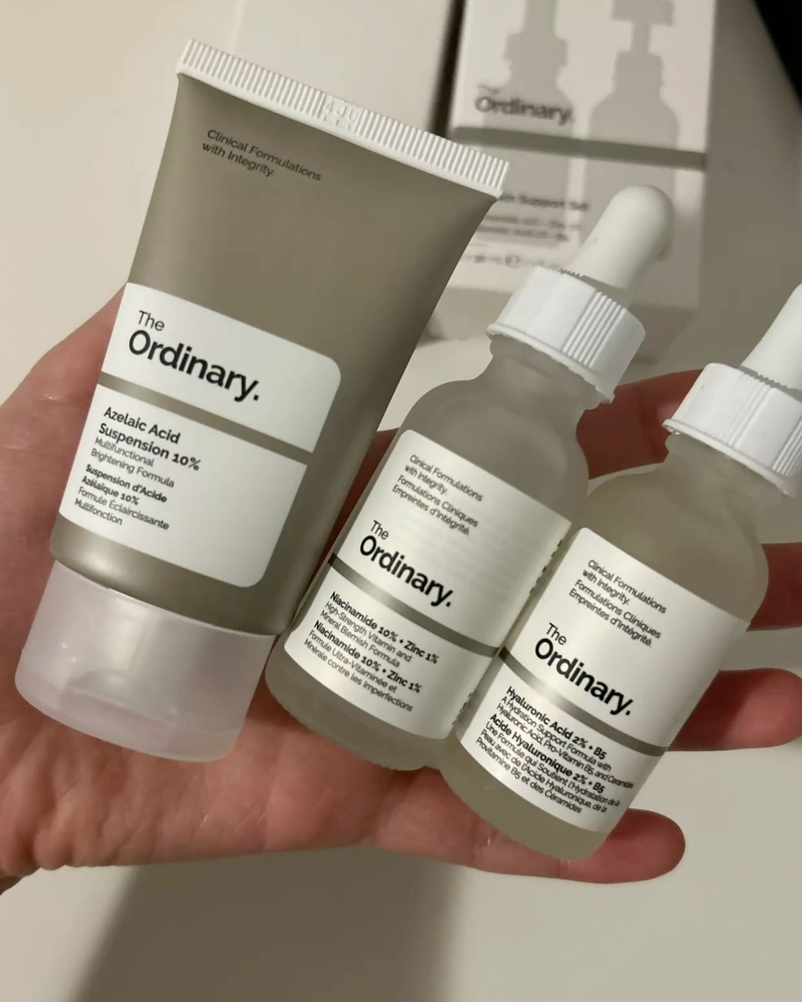 Hand holding a tube of The Ordinary Azelaic Acid Suspension 10% beside two dropper bottles
