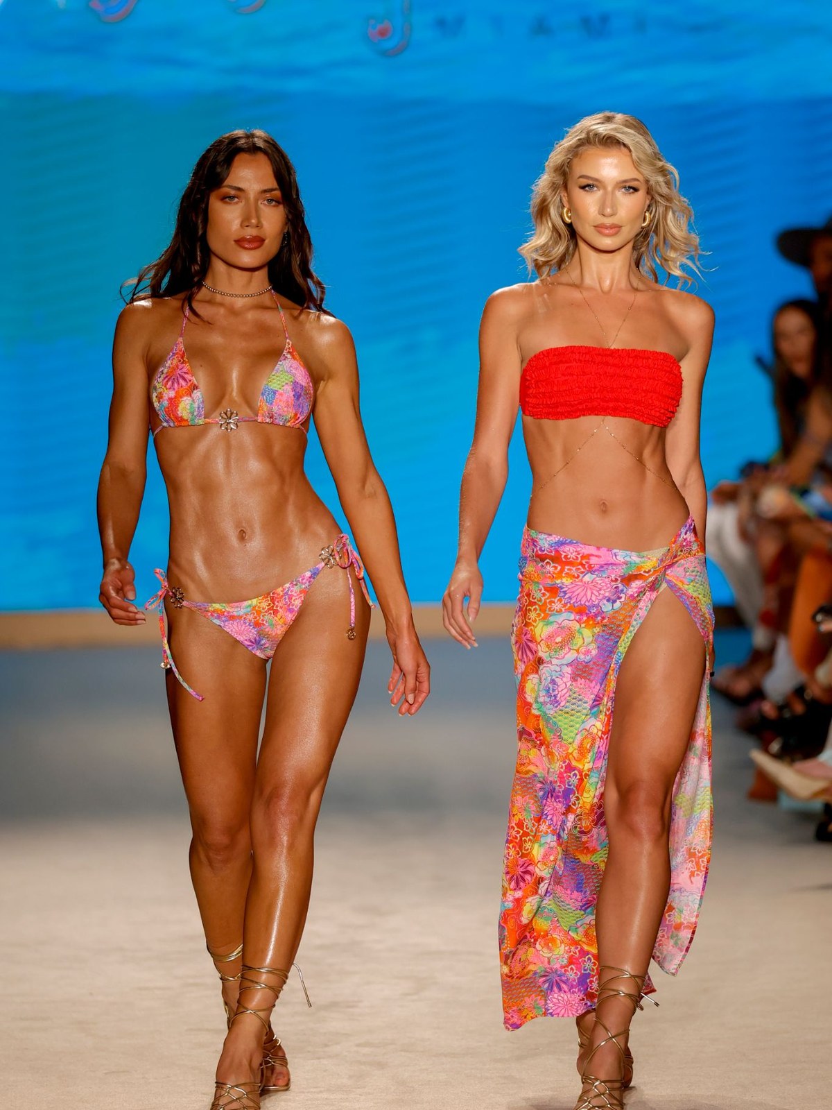 Two models in bright swimwear walking a Luli Fama runway