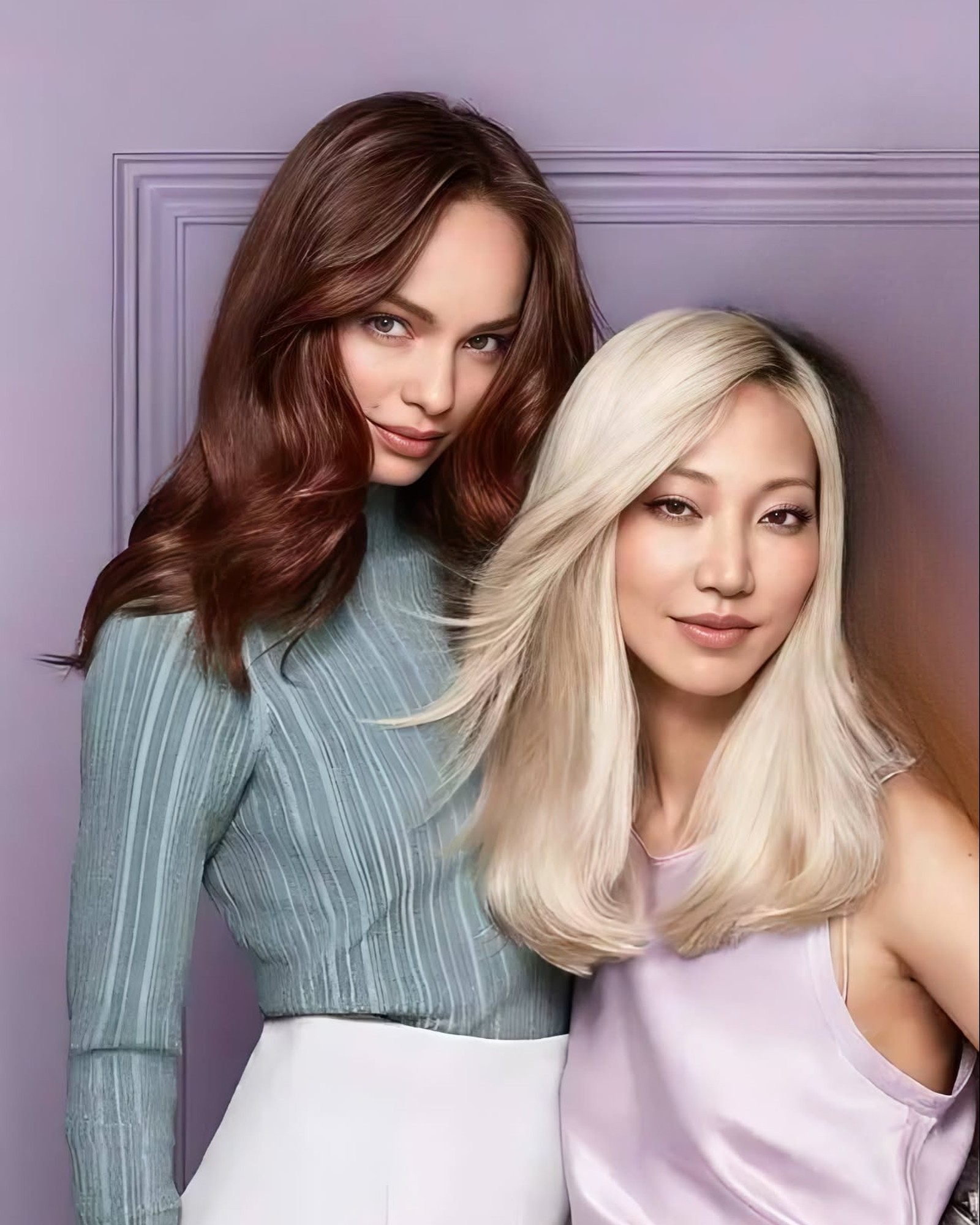 Two women against a lilac wall, one with long glossy auburn hair and one with sleek platinum blonde hair
