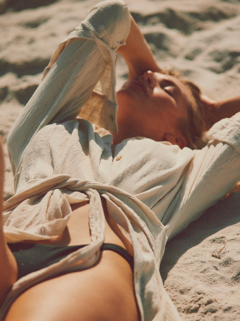 Model reclining in pale resortwear on a beach