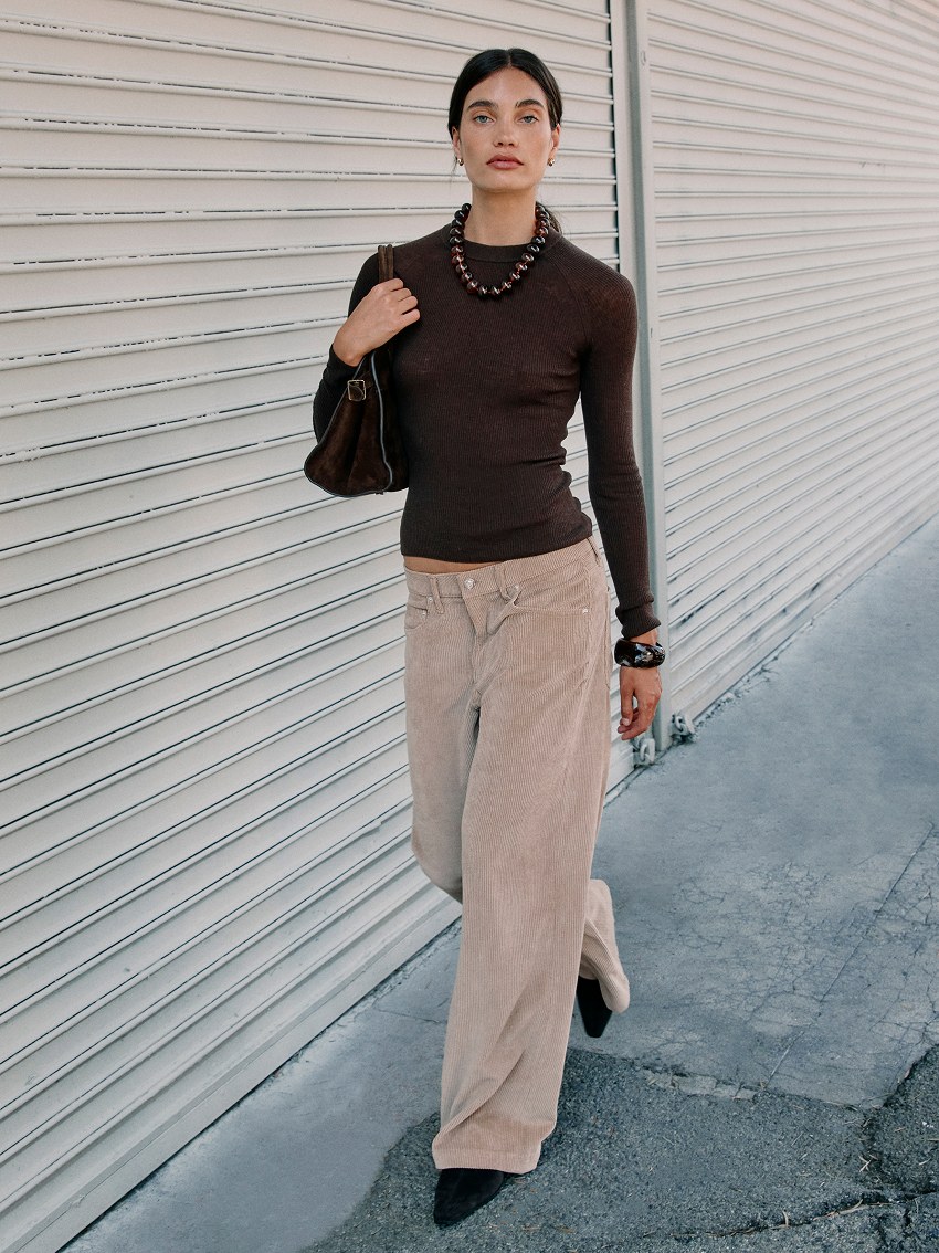 Model in a dark knit and pale trousers walking beside a roll-up street door