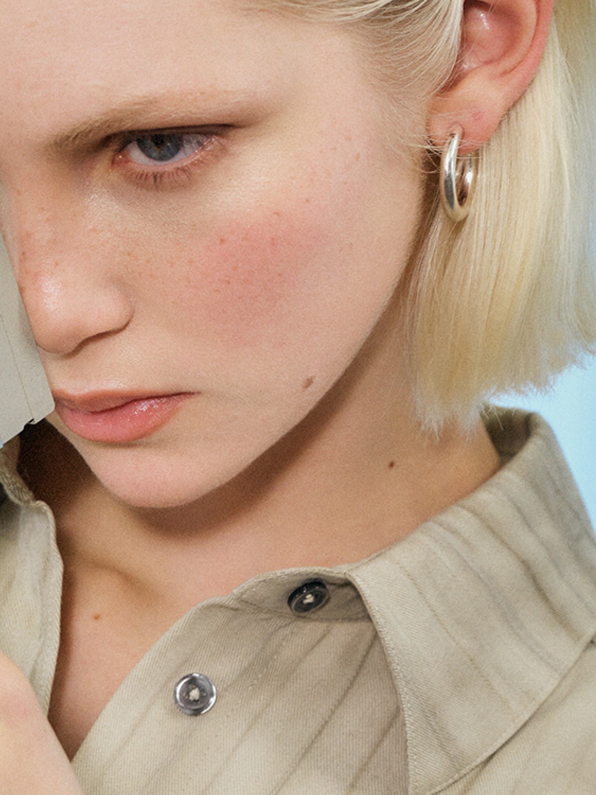 Close portrait of a blonde model in a light shirt against a blue-lit studio backdrop