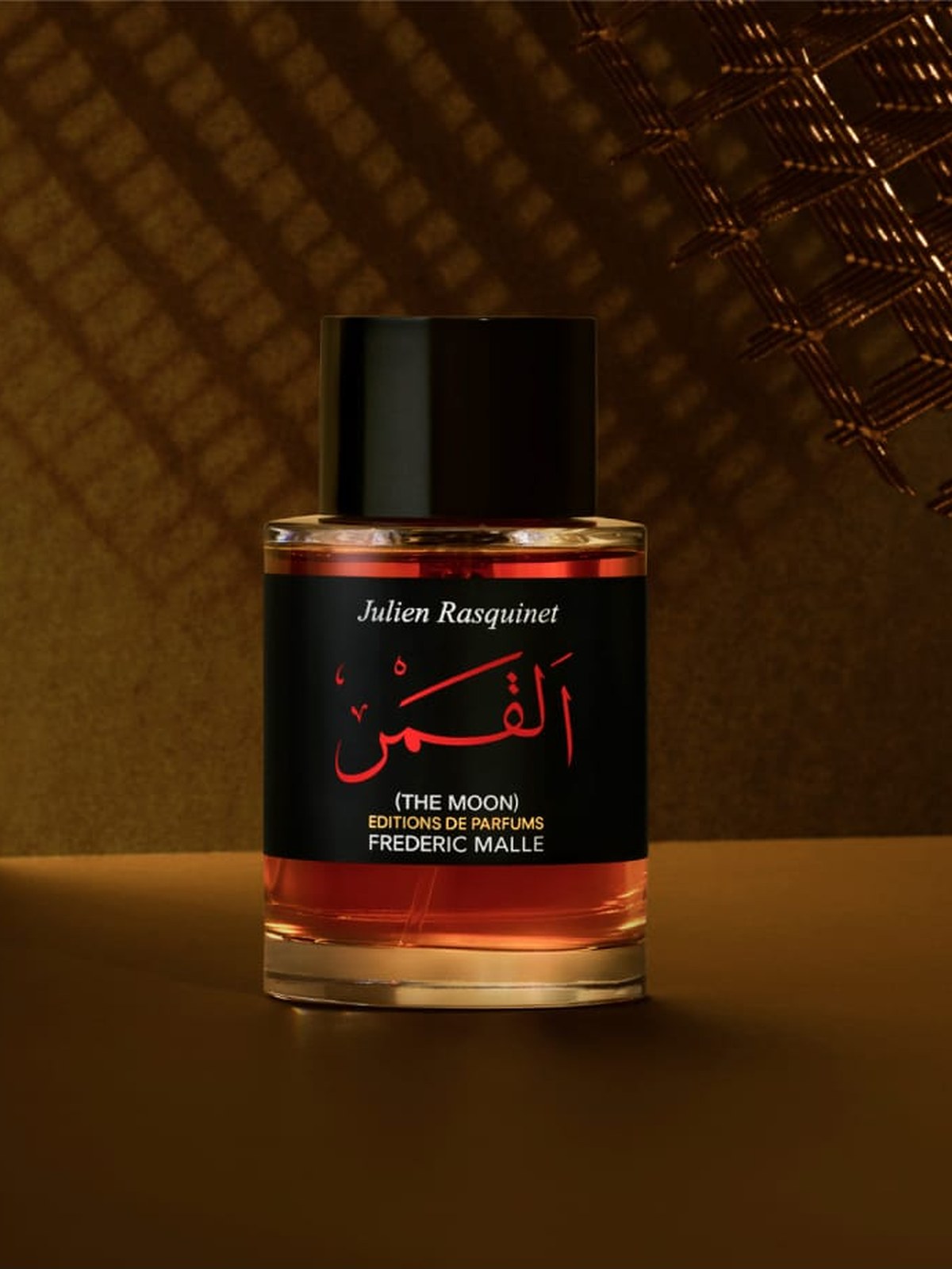 Fragrance bottle in warm amber light beneath a brass mesh canopy