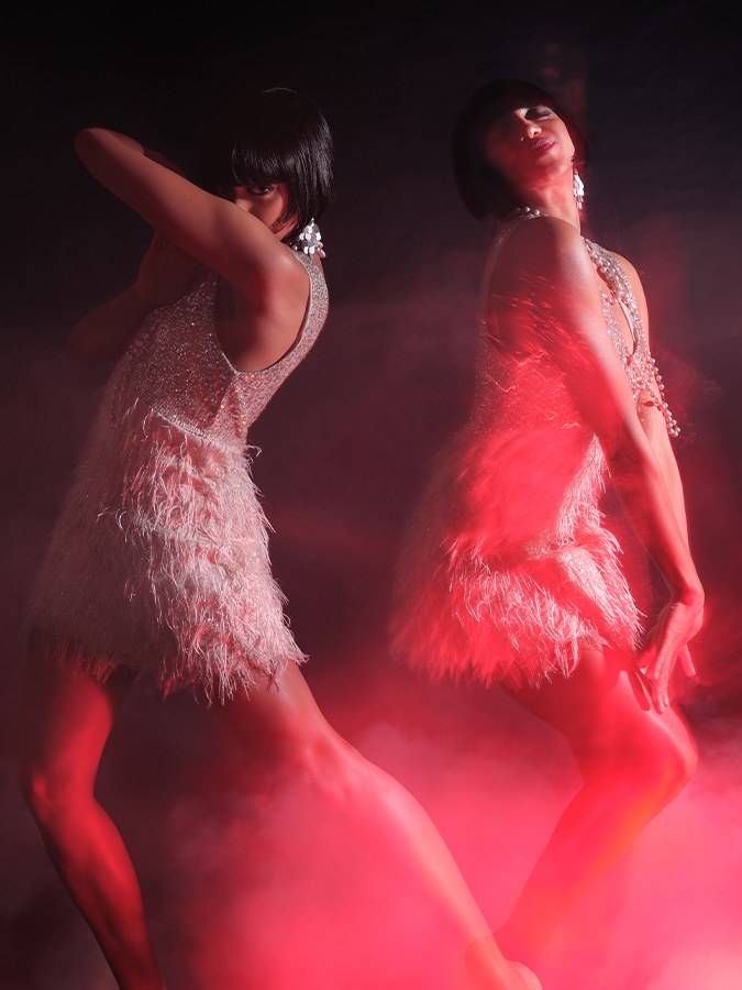 Two dancers in feathered dresses move through pink-red haze in the Sparkling Jo launch story