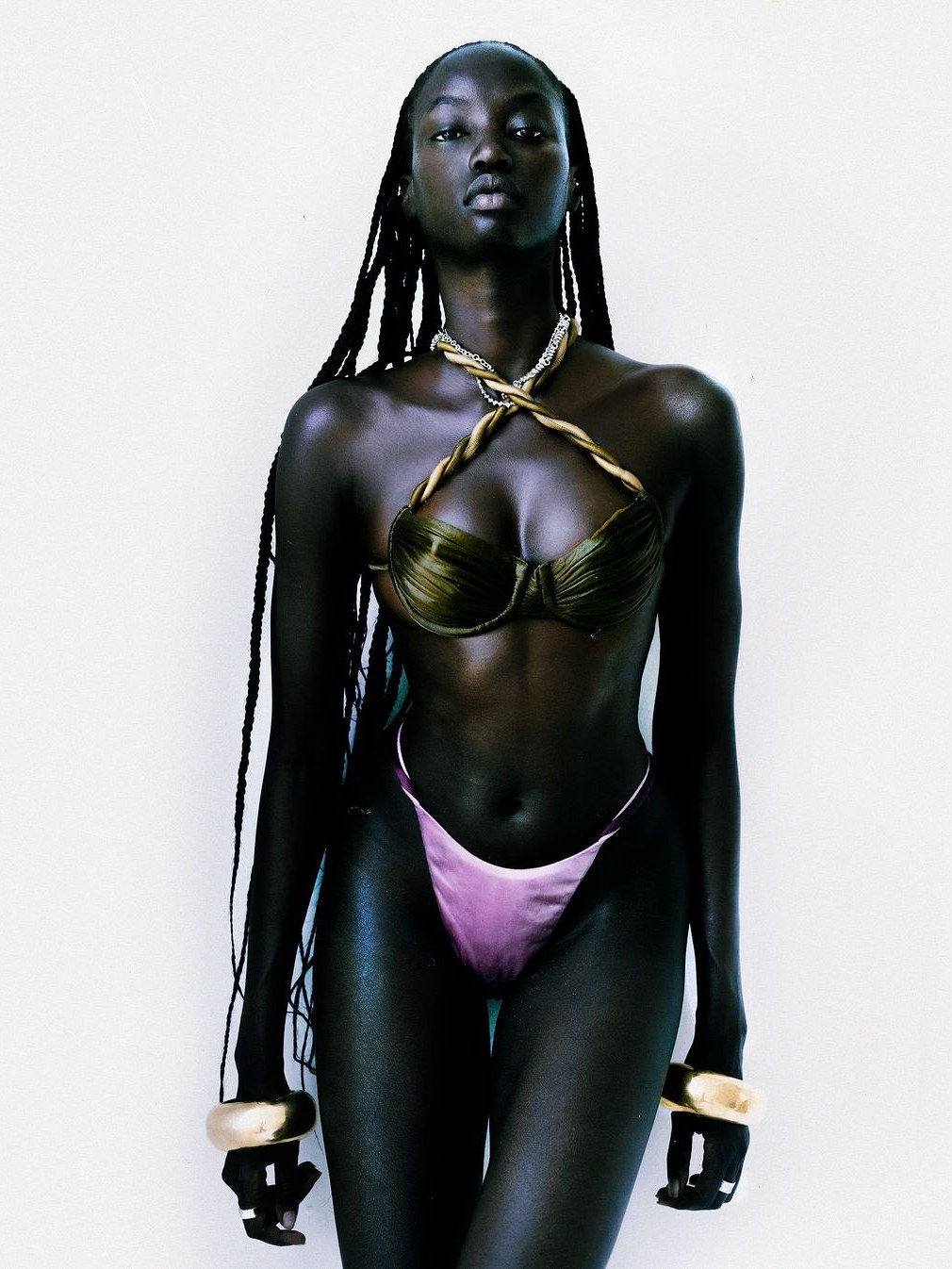 Model in a green draped bikini against a pale studio backdrop