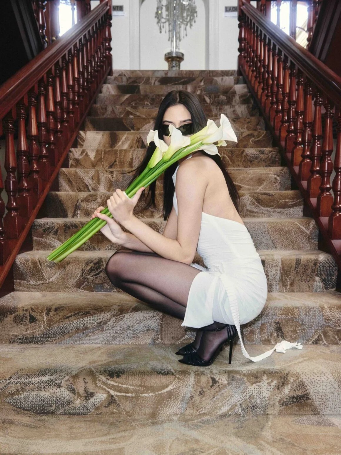 Model in a short white dress seated on a staircase