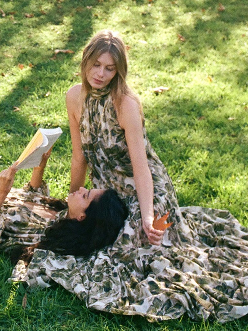 Two models in printed dresses relaxing together on a green lawn