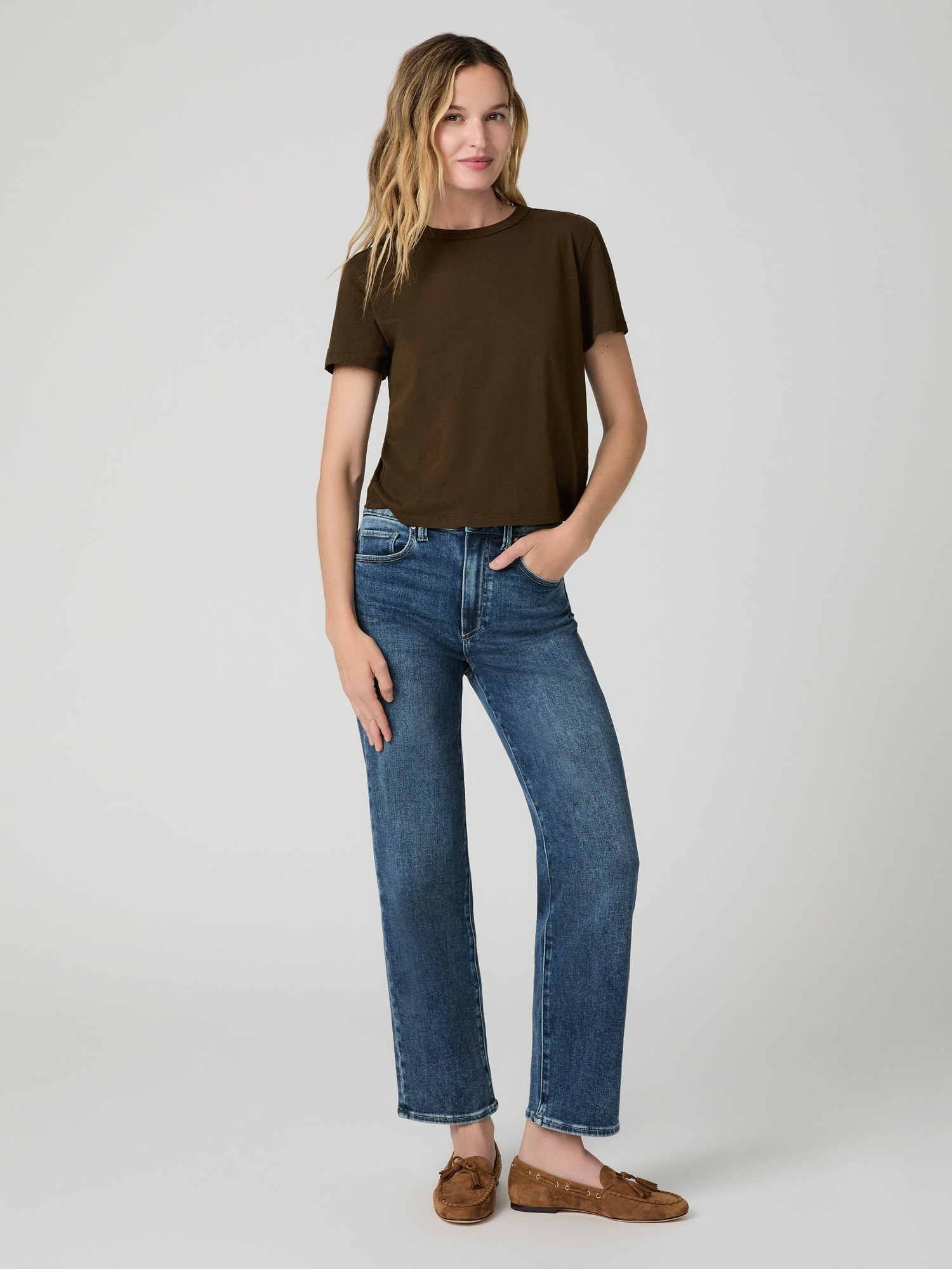 Model in a brown t shirt and mid wash straight jeans with a hand in her pocket