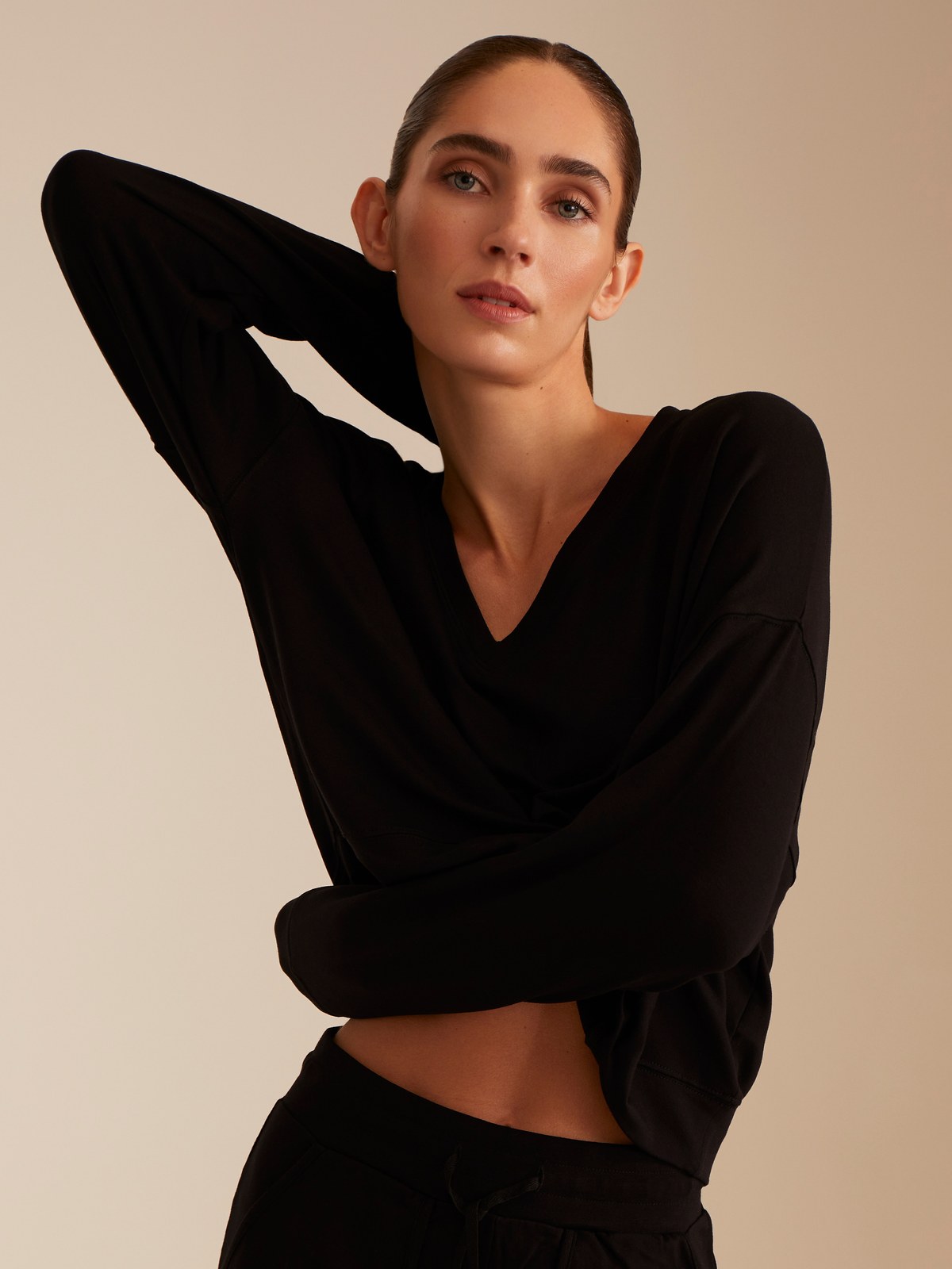 Woman in a black TKEES top against a warm studio backdrop
