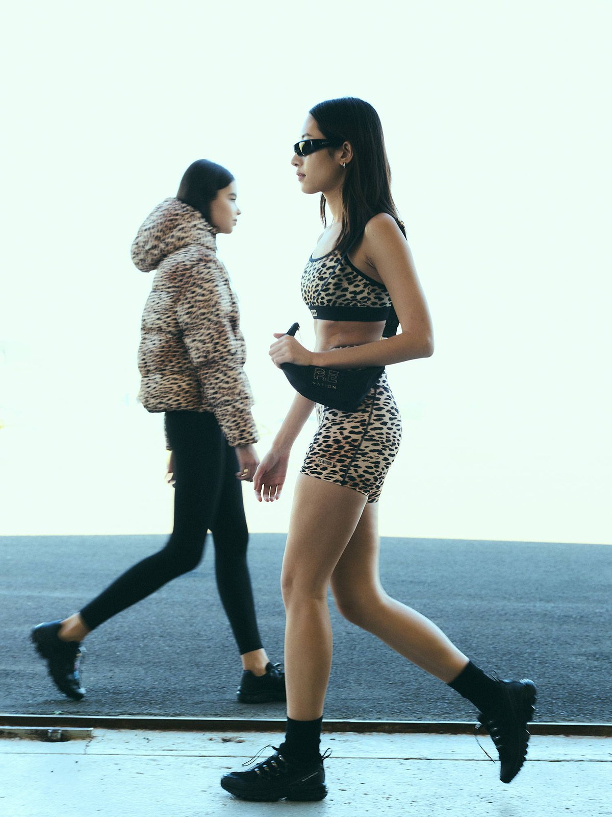Two models walking near a plane in patterned and neutral activewear