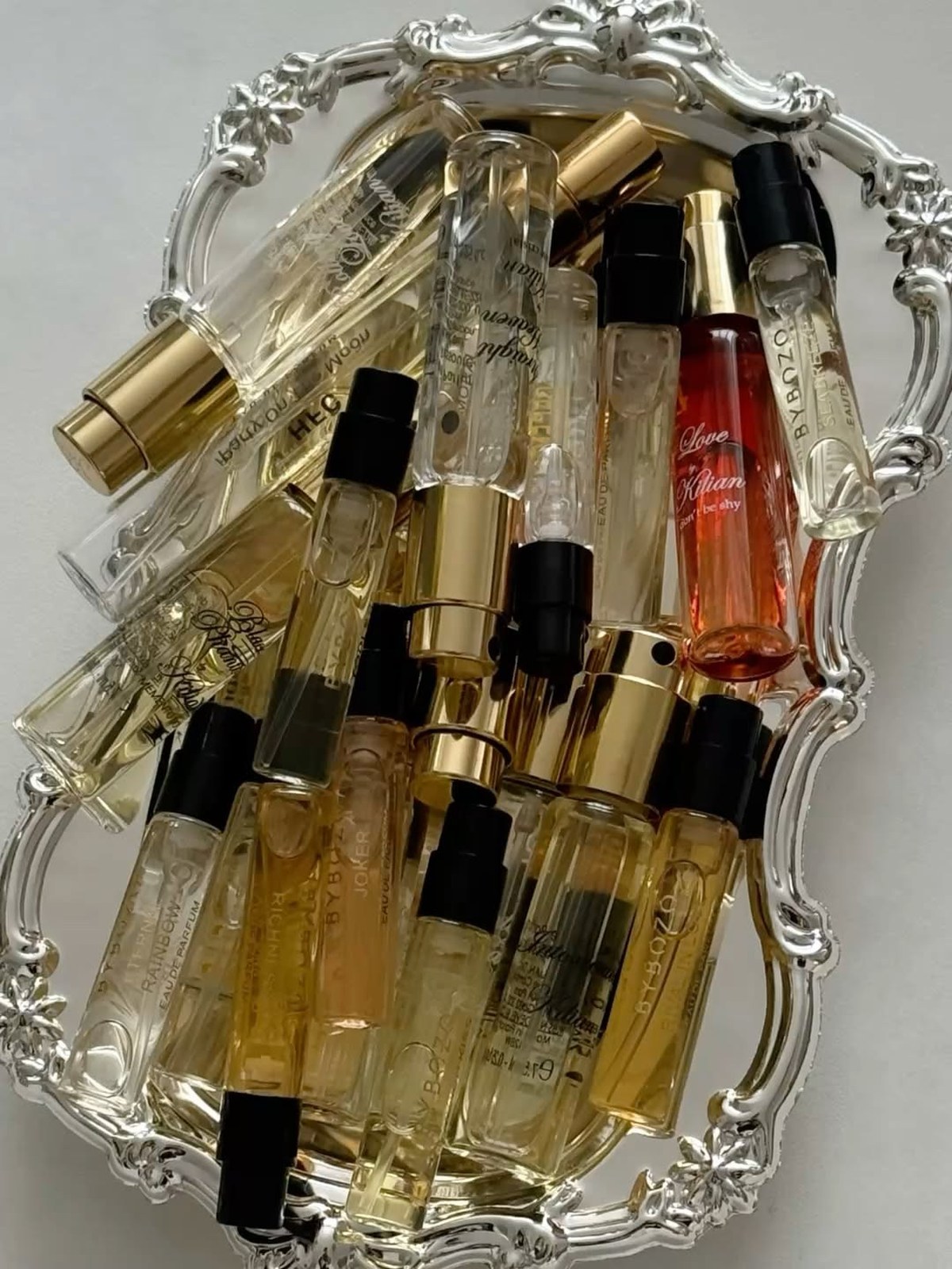 Pile of small perfume sample vials with gold and black caps on an ornate silver tray