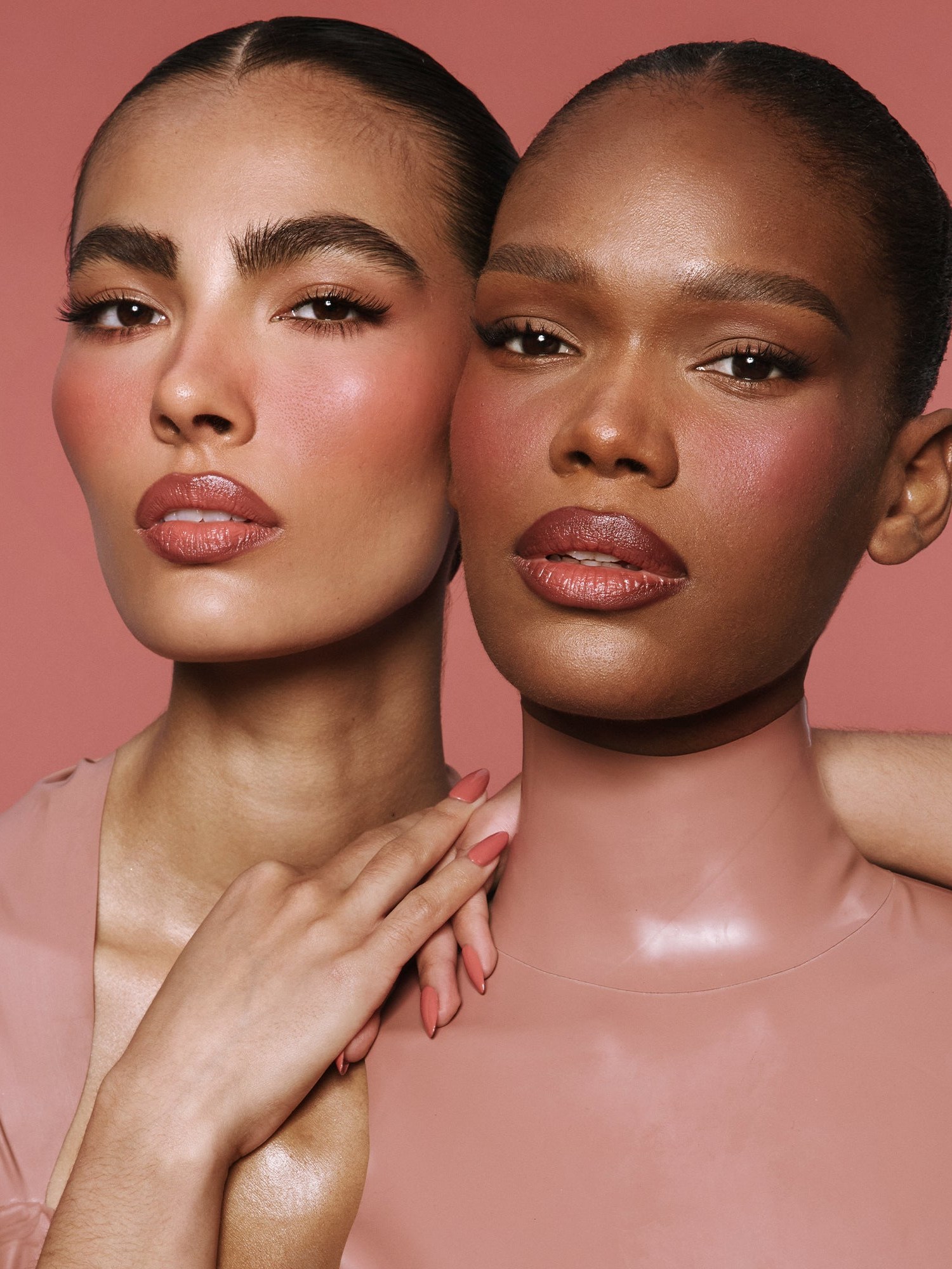 Two models with rosy blush and glossy skin on a dusty rose backdrop