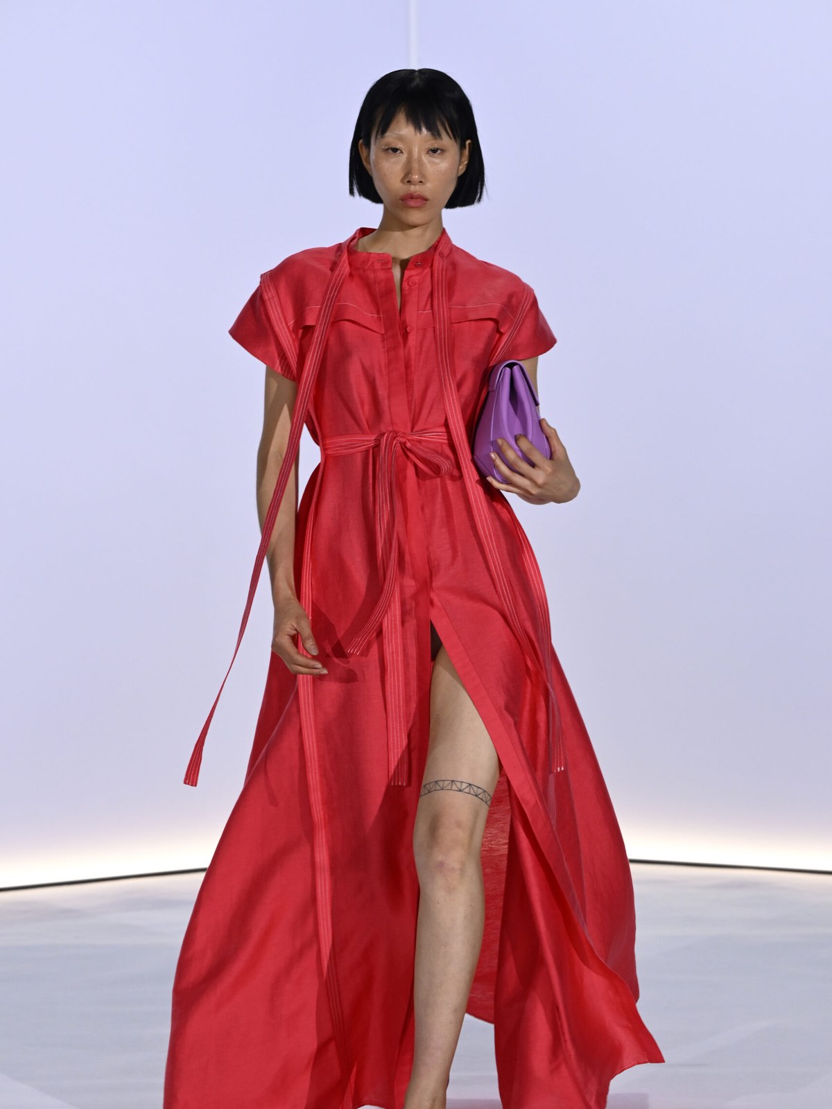 Model in a vivid red dress carrying a purple clutch on the runway