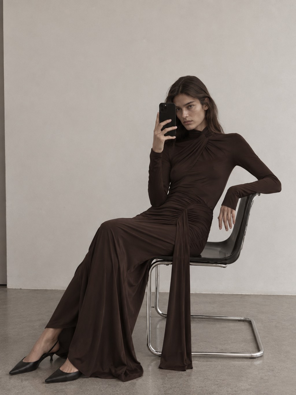 Model seated in a dark draped jersey dress in a spare studio