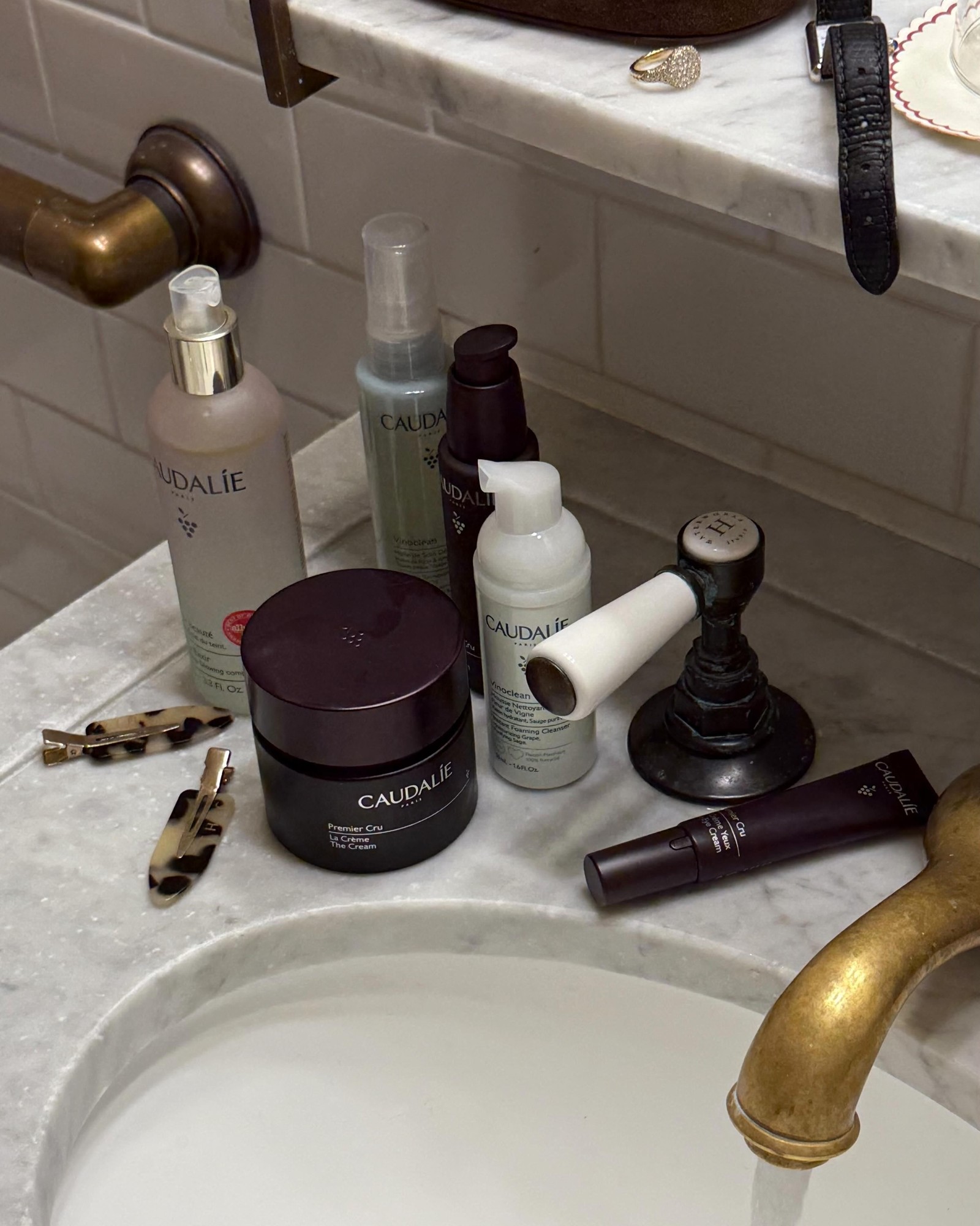 Marble bathroom sink with Caudalie cleanser, cream and eye cream bottles beside a brass faucet