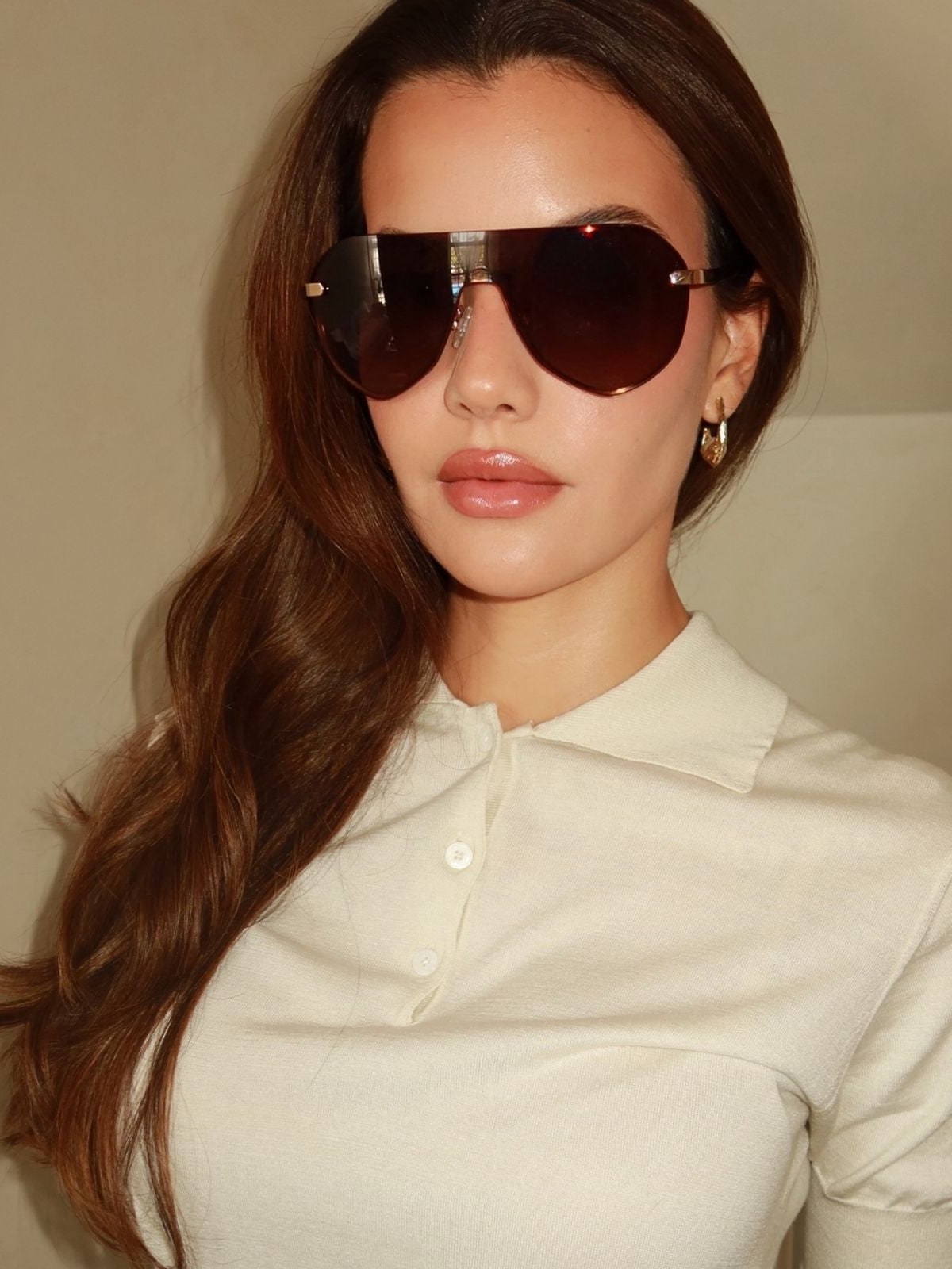 Model in a cream polo wearing DIFF aviator sunglasses in a warm studio