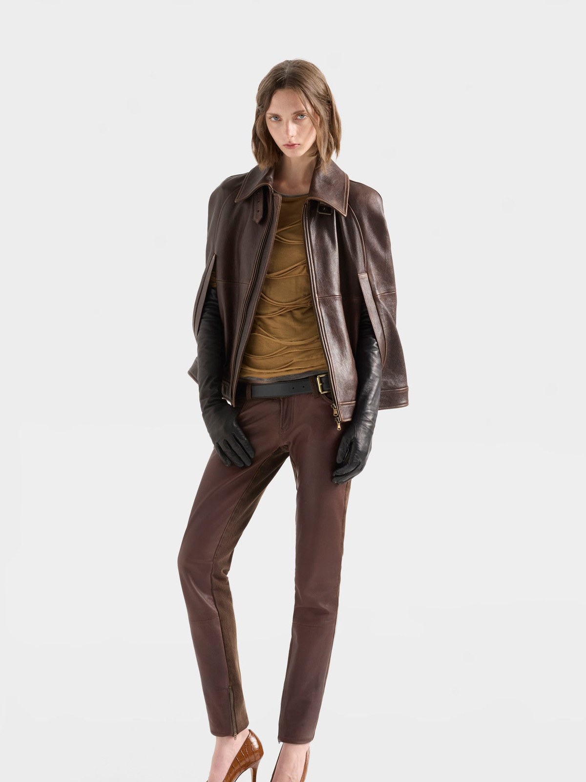 Model in a brown leather cape jacket and brown skinny trousers with heels