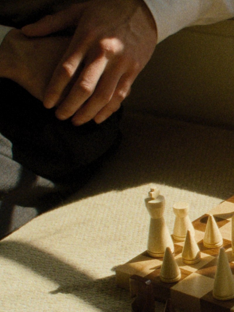 A hand reaches toward a wooden chessboard in a warm interior