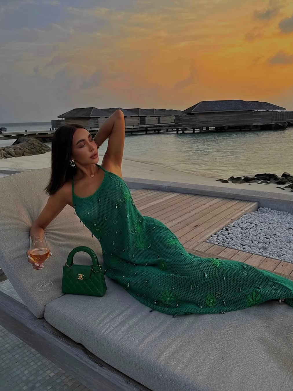 Woman in an emerald green gown reclining beside the water at sunset