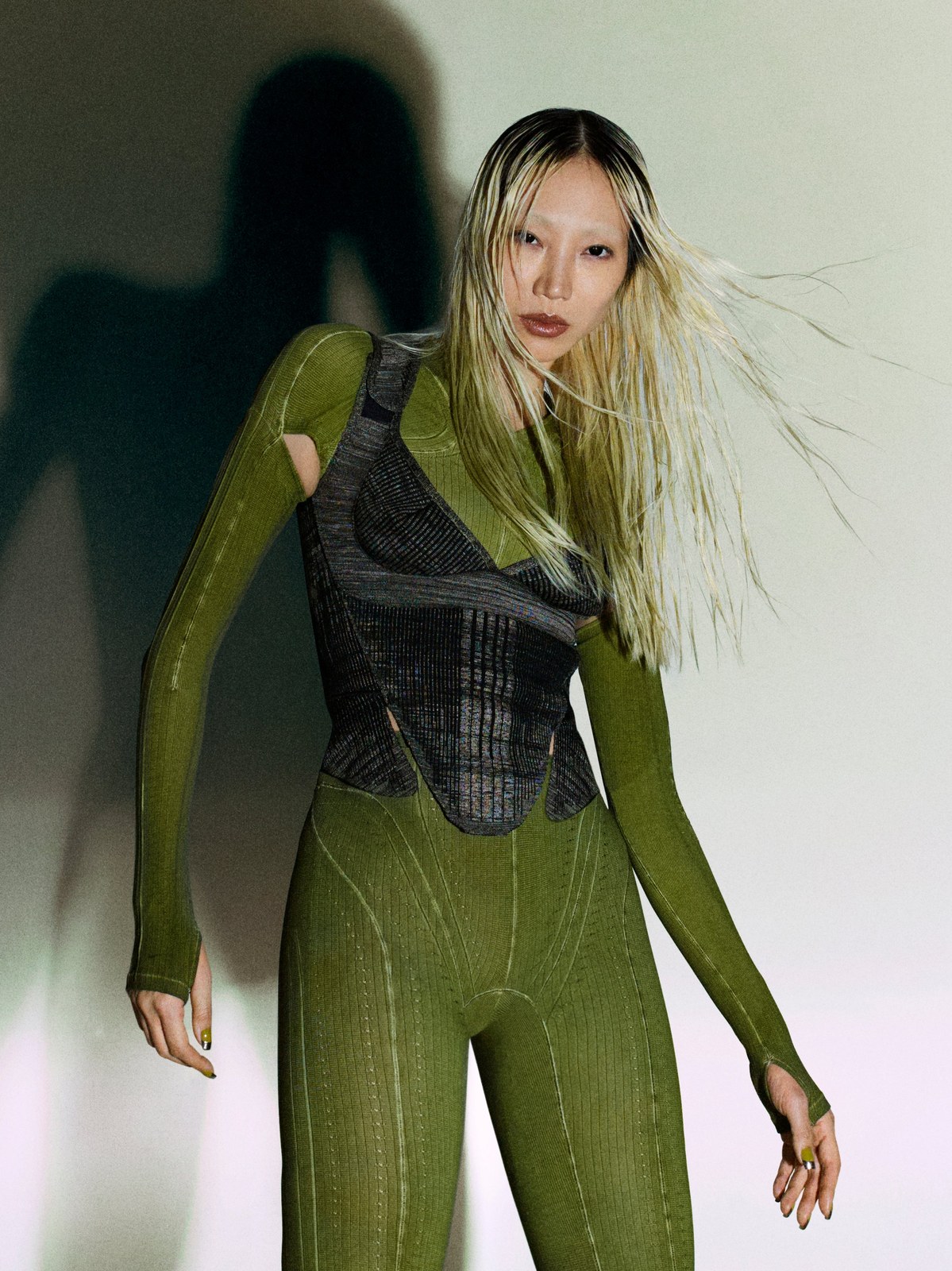 Model in a green corsetry-inspired look in a shadowed studio