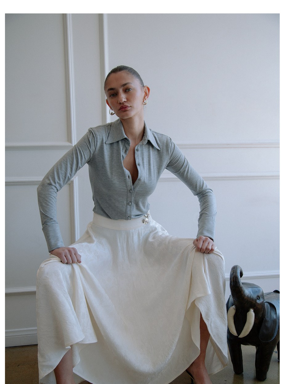 Model seated in a grey button front top and flowing white skirt