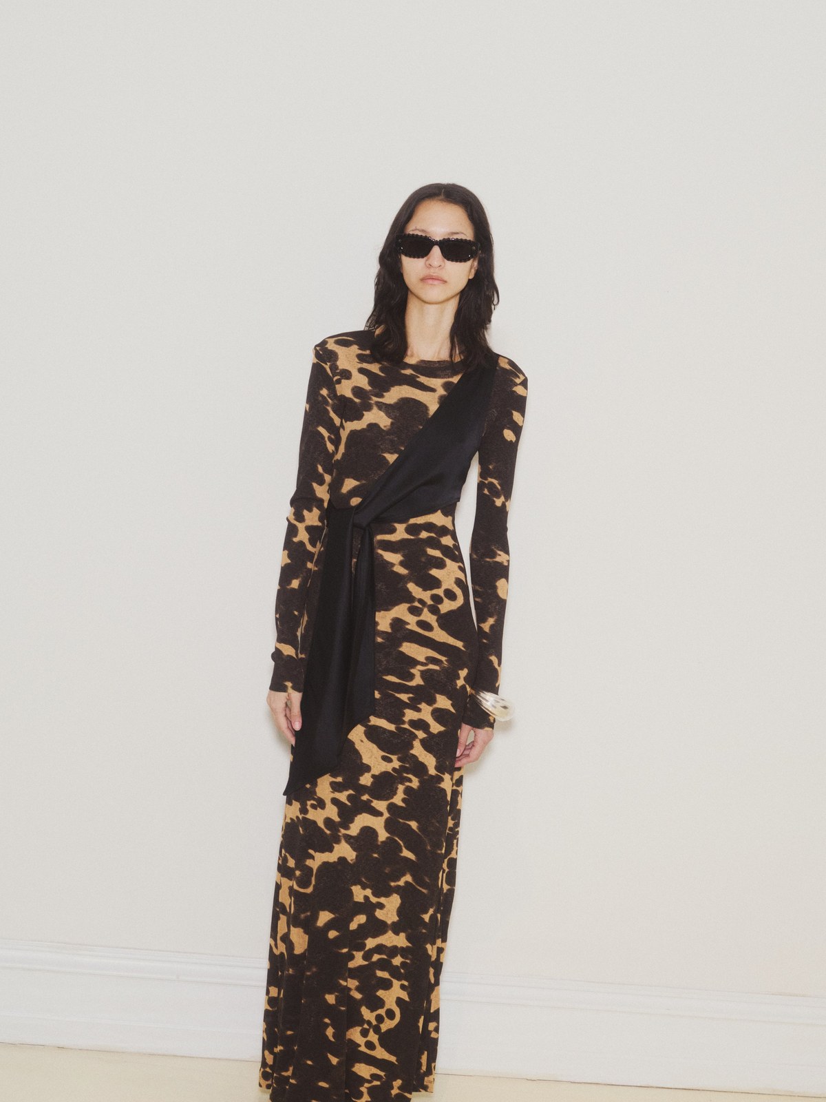 Model in a dark abstract print dress against a pale studio ground