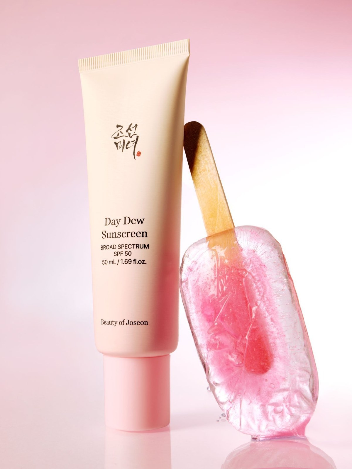 Beauty of Joseon Day Dew Sunscreen SPF 50 tube leaning against a pink ice pop on a pink gradient background