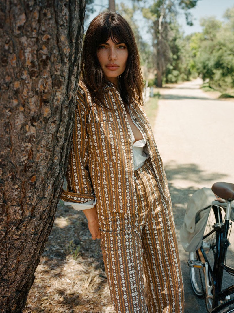 Woman in a patterned outfit beside a bicycle on a tree-lined path