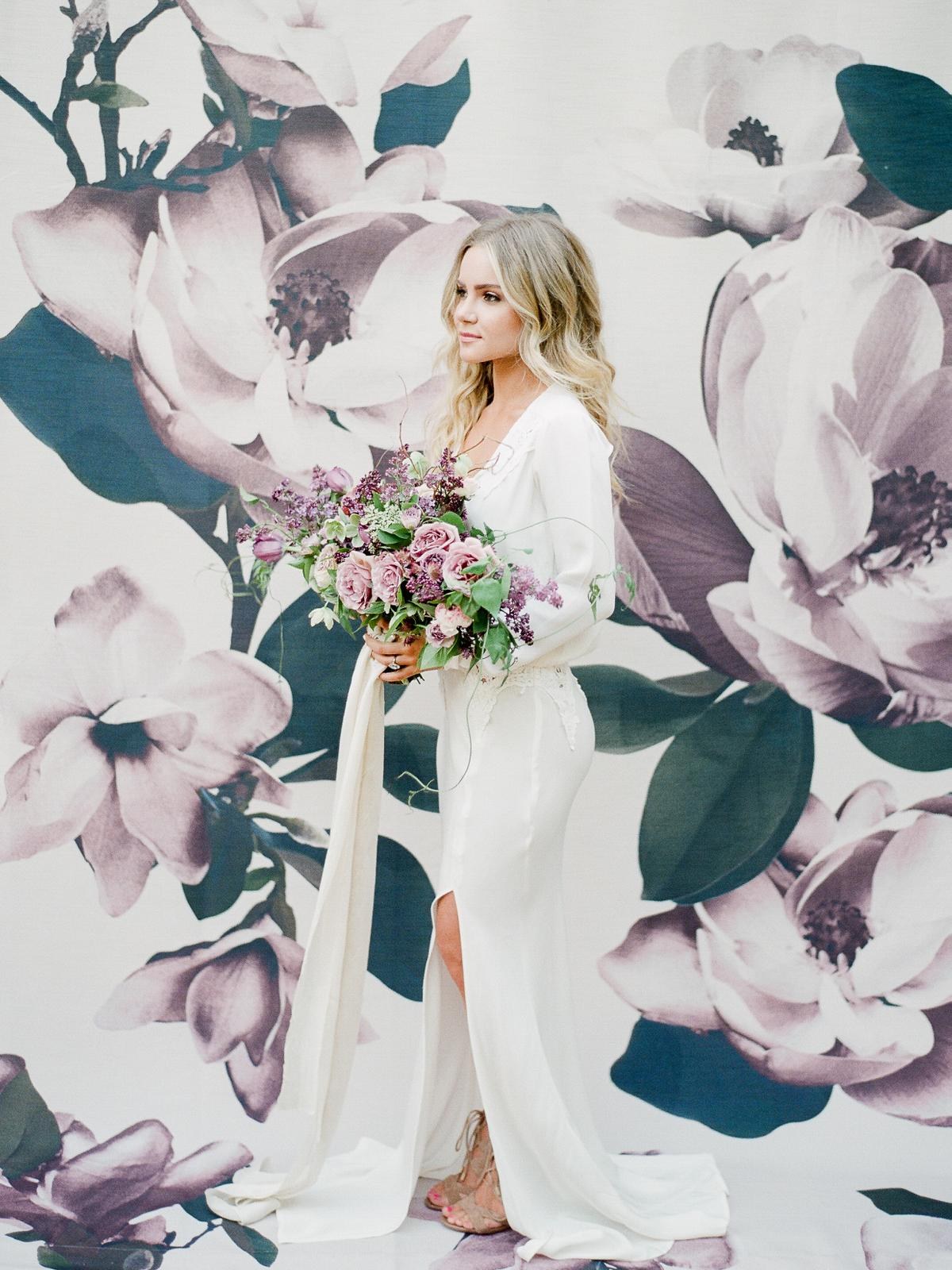 Model in a white Stone Cold Fox bridal gown against a floral backdrop
