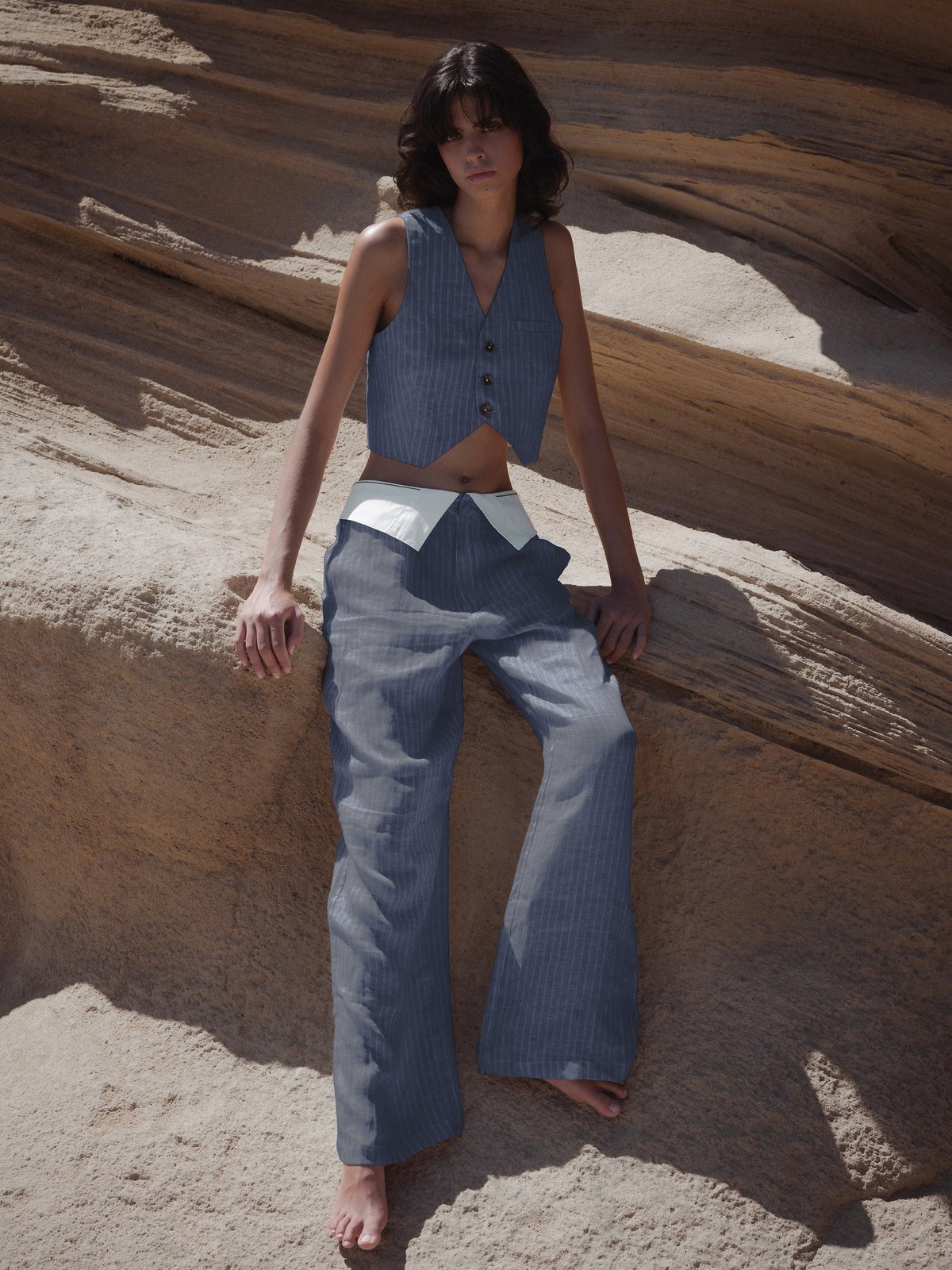 Model in a pale blue vest and wide trousers among desert rock formations