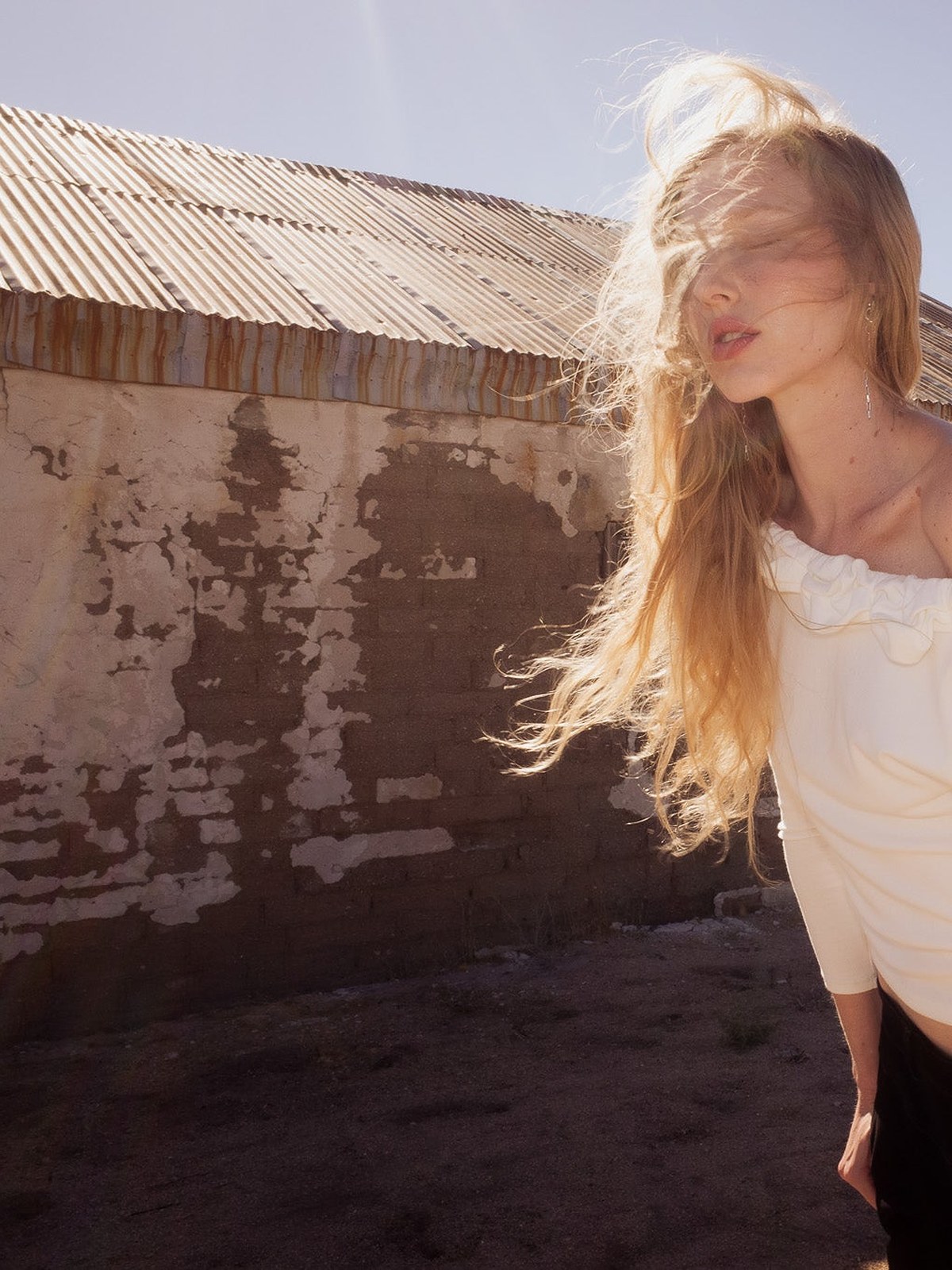 Model with windswept hair in a white ruffled knit top and black trousers in the desert