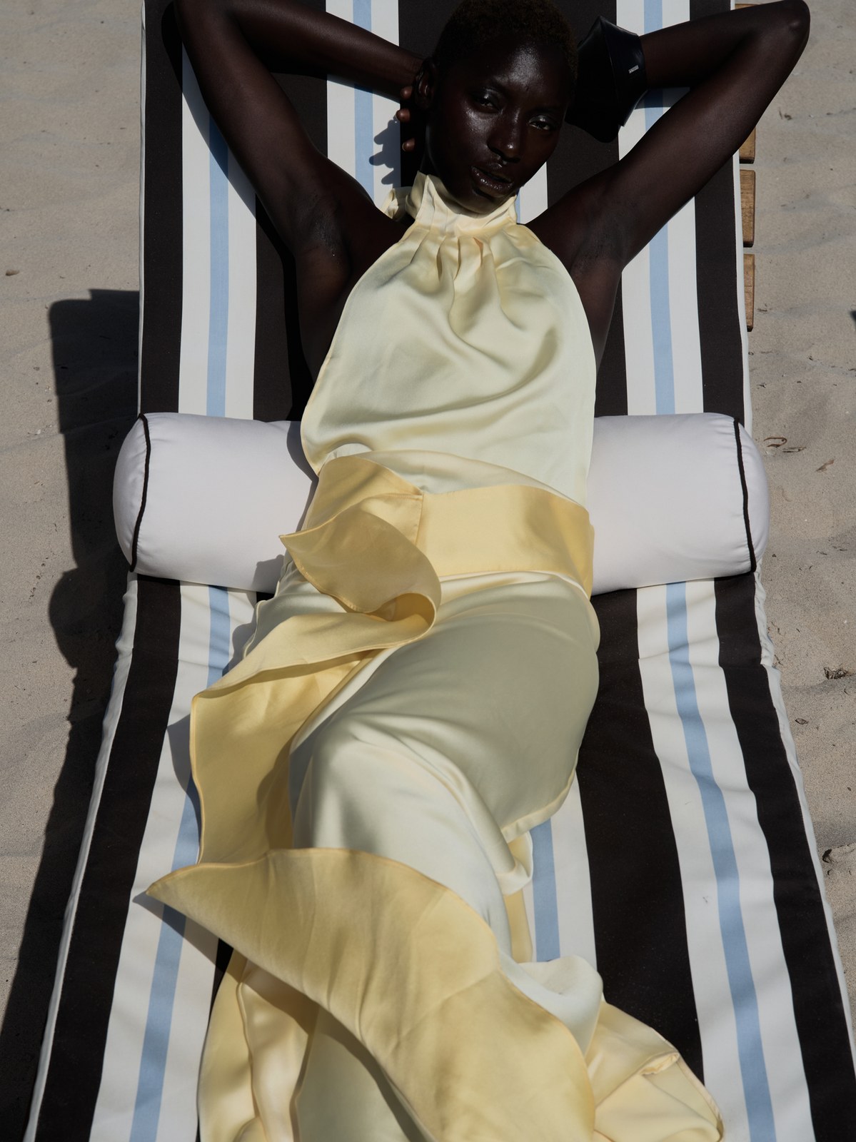 Model reclining in an ivory halter dress on a striped outdoor lounger