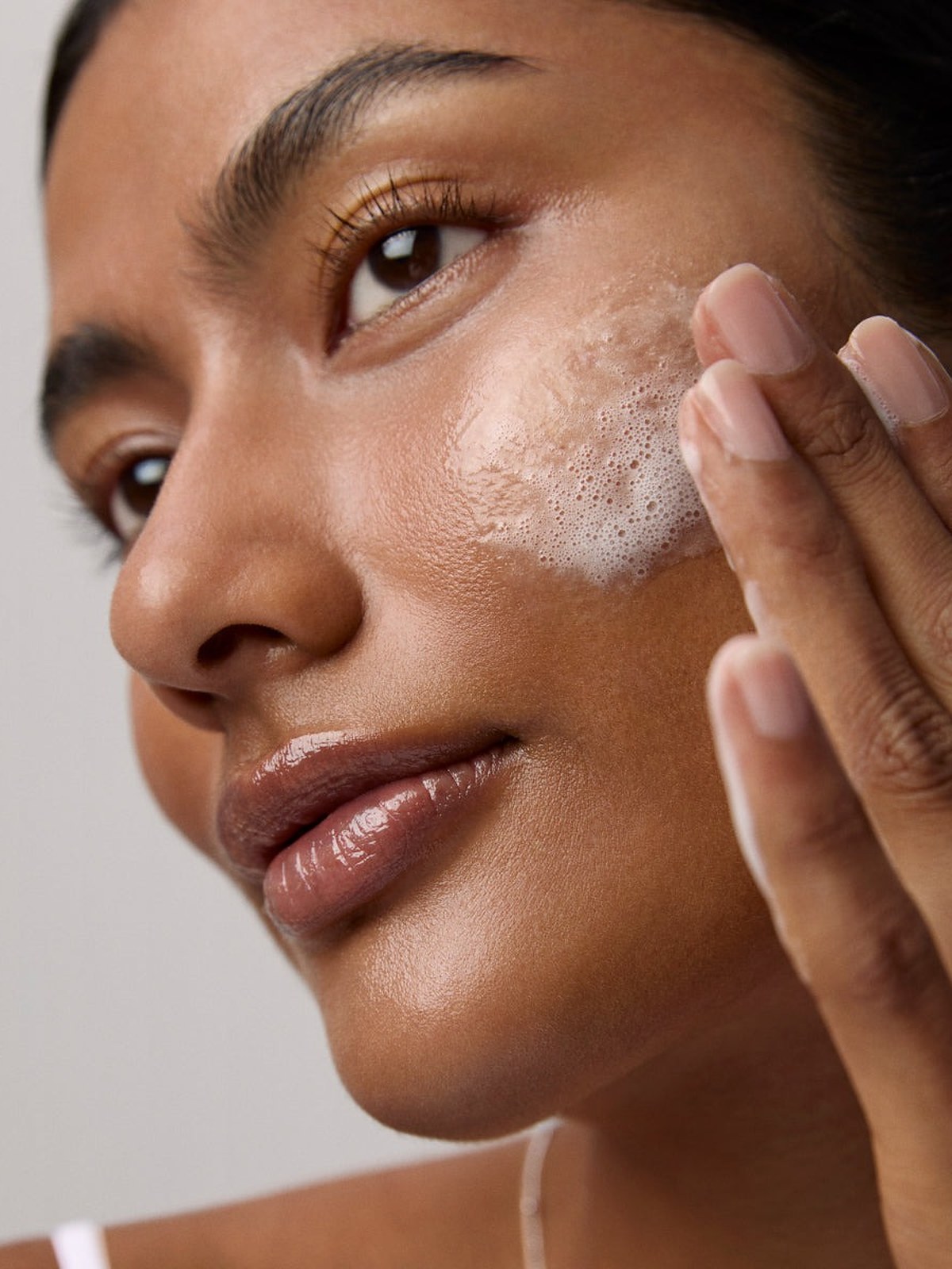 Model washing her face with soft foam on her cheek