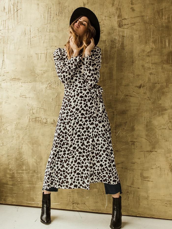 Woman in a leopard print dress and black hat against a textured wall