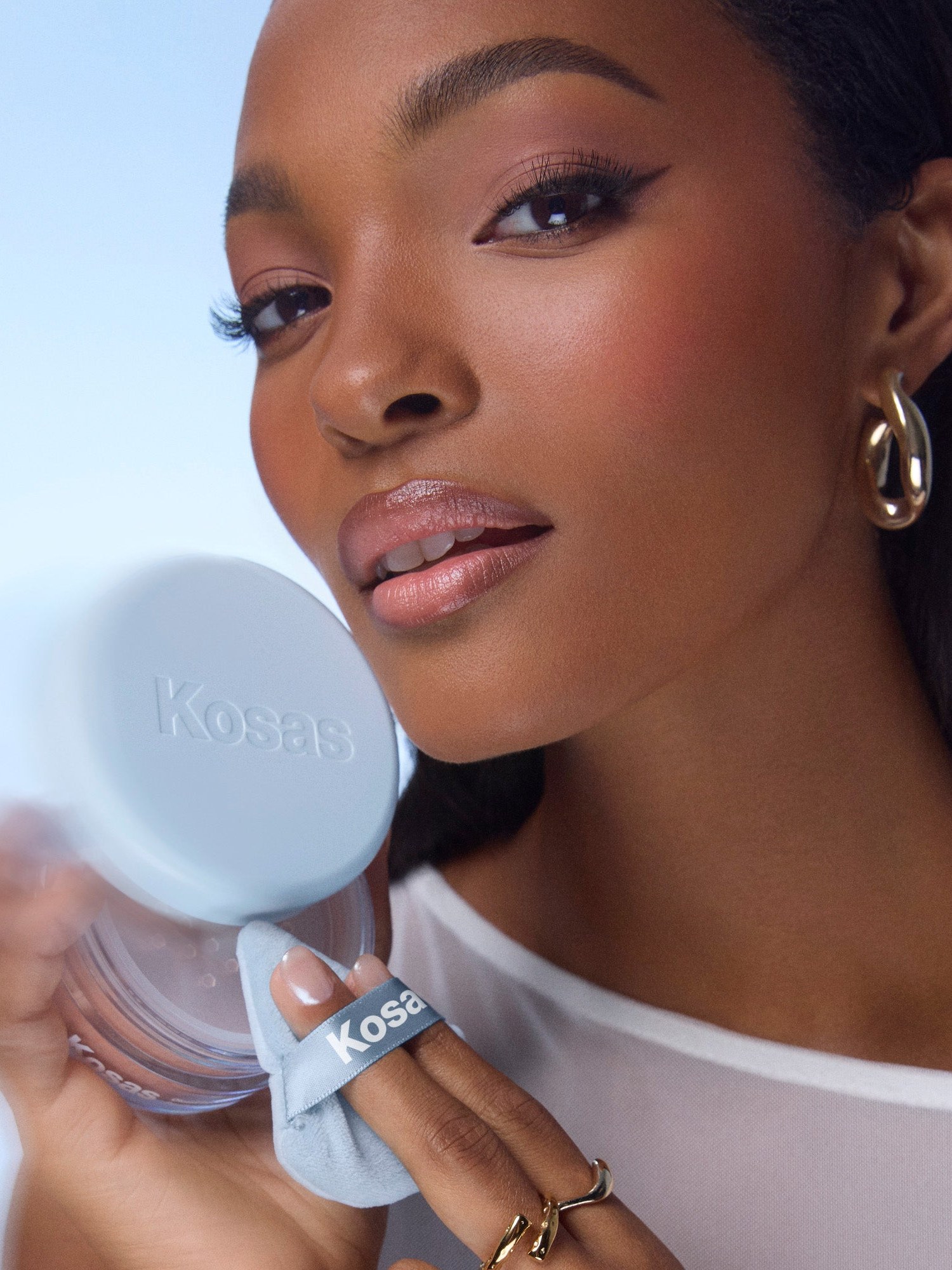 Model holding a Kosas powder jar and puff against a soft blue background