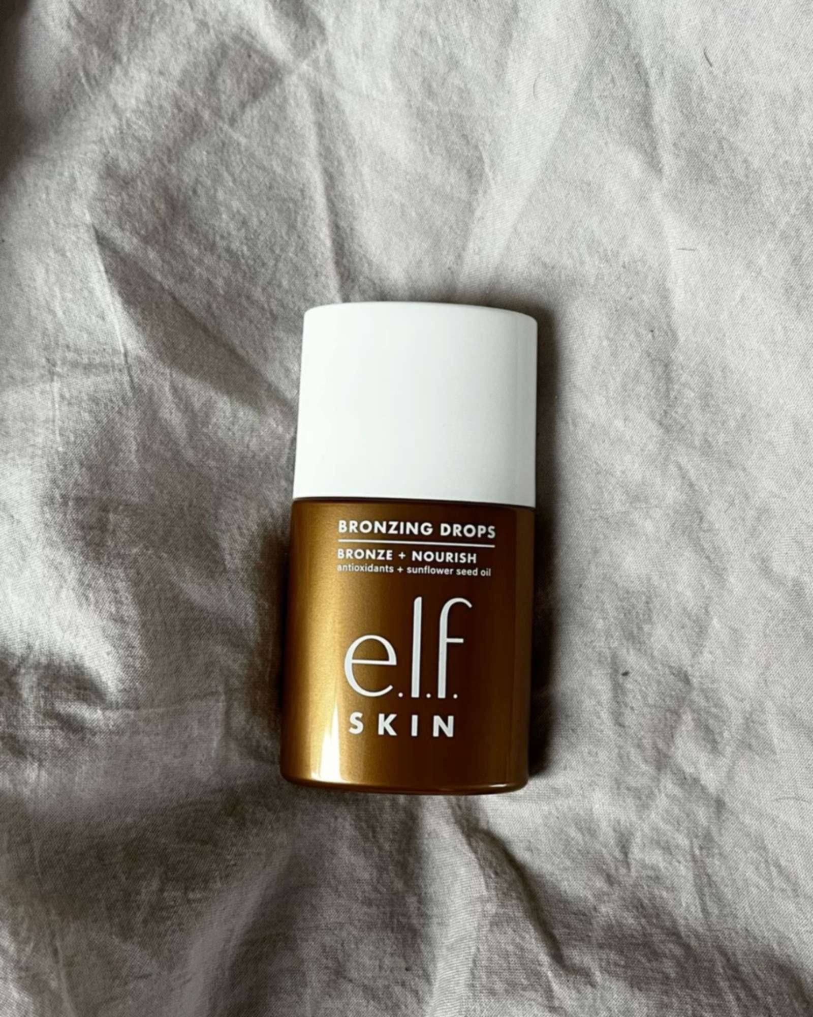Bottle of e.l.f. SKIN Bronzing Drops with a white cap lying on rumpled gray linen
