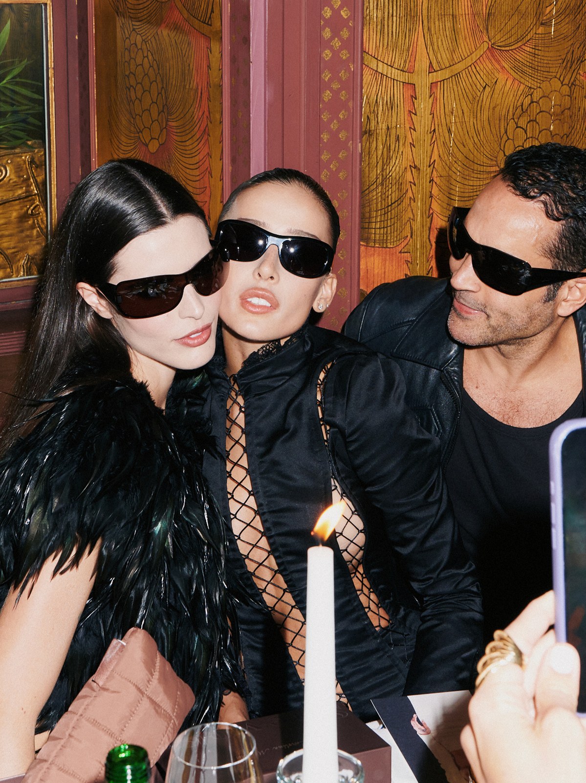 Two women and a man wearing sunglasses together at a warmly lit dinner