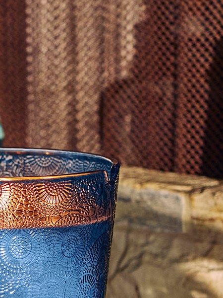 Close detail of a blue textured candle vessel against a stone table and woven backdrop