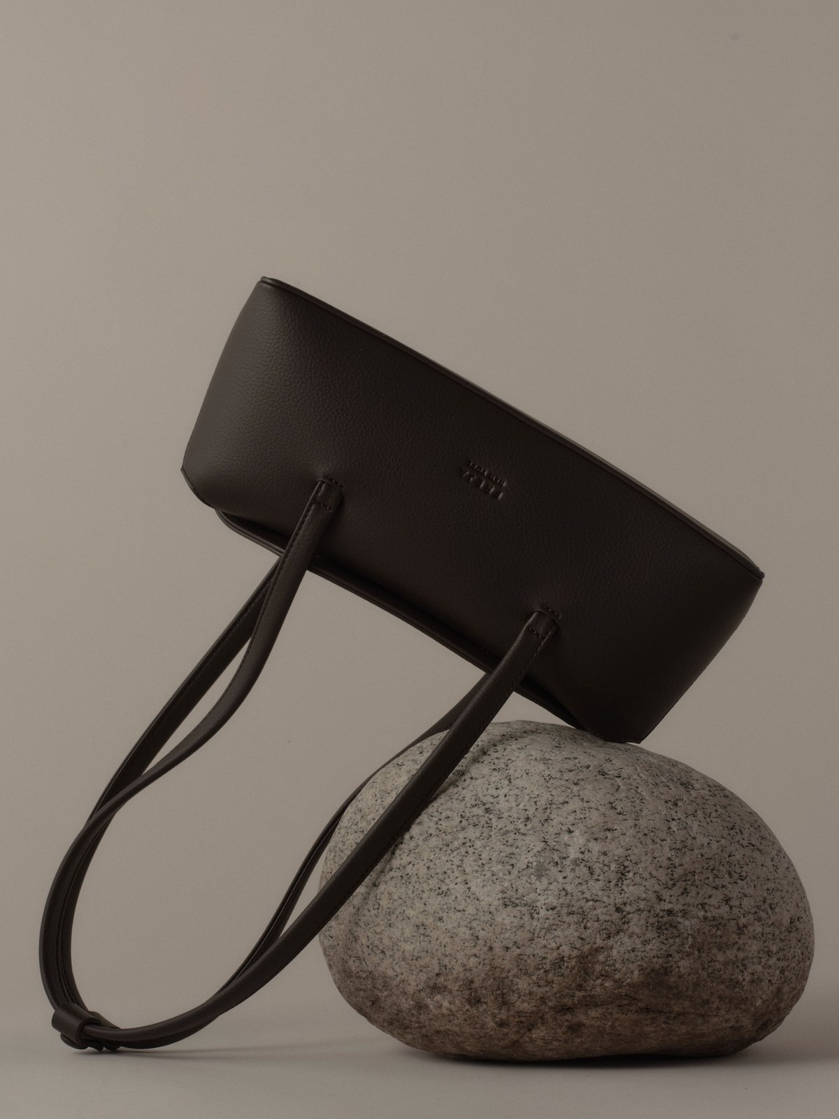 Black Freja tote balanced on a stone against a taupe backdrop