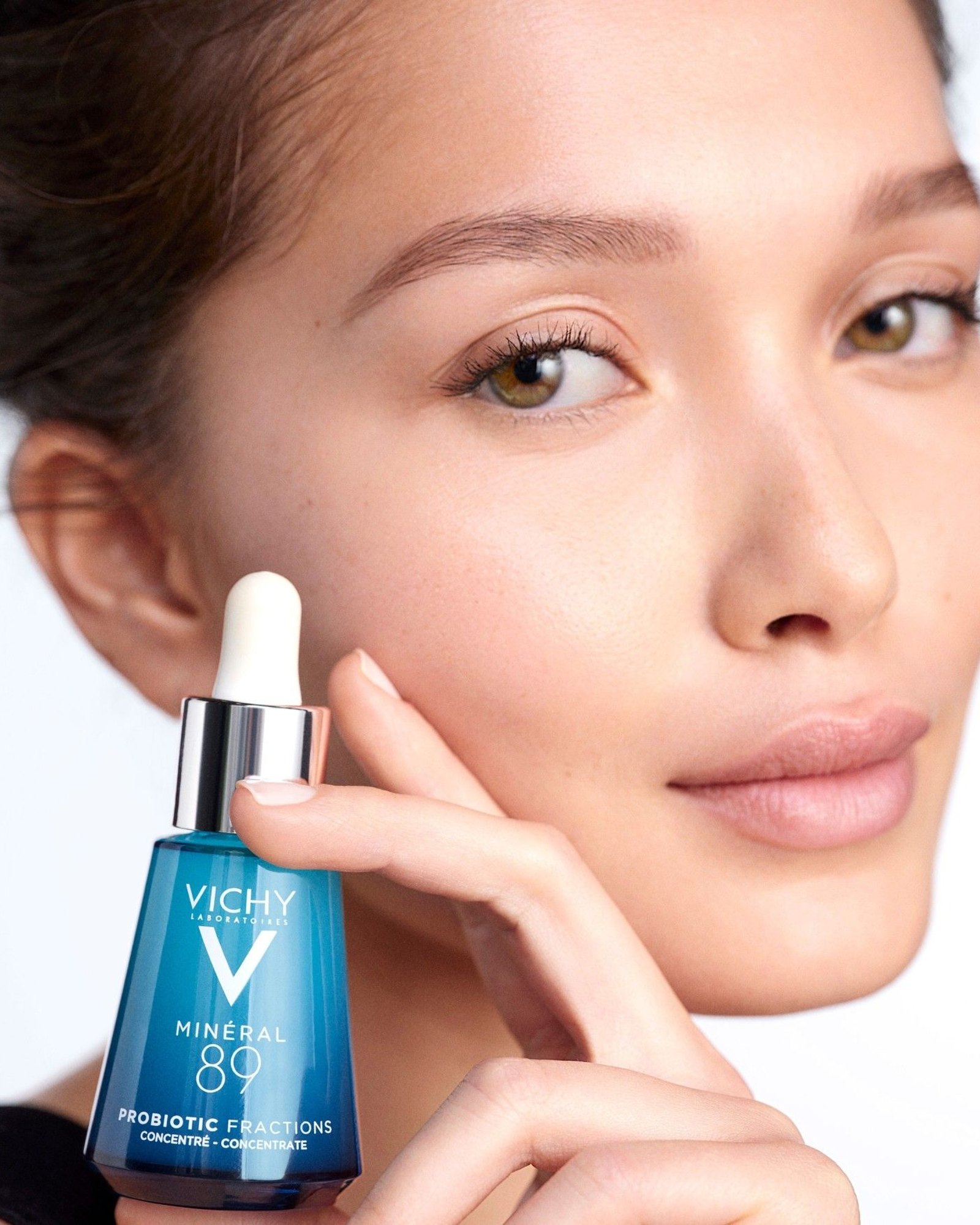 Woman holding a blue Vichy Mineral 89 Probiotic Fractions dropper bottle against her cheek