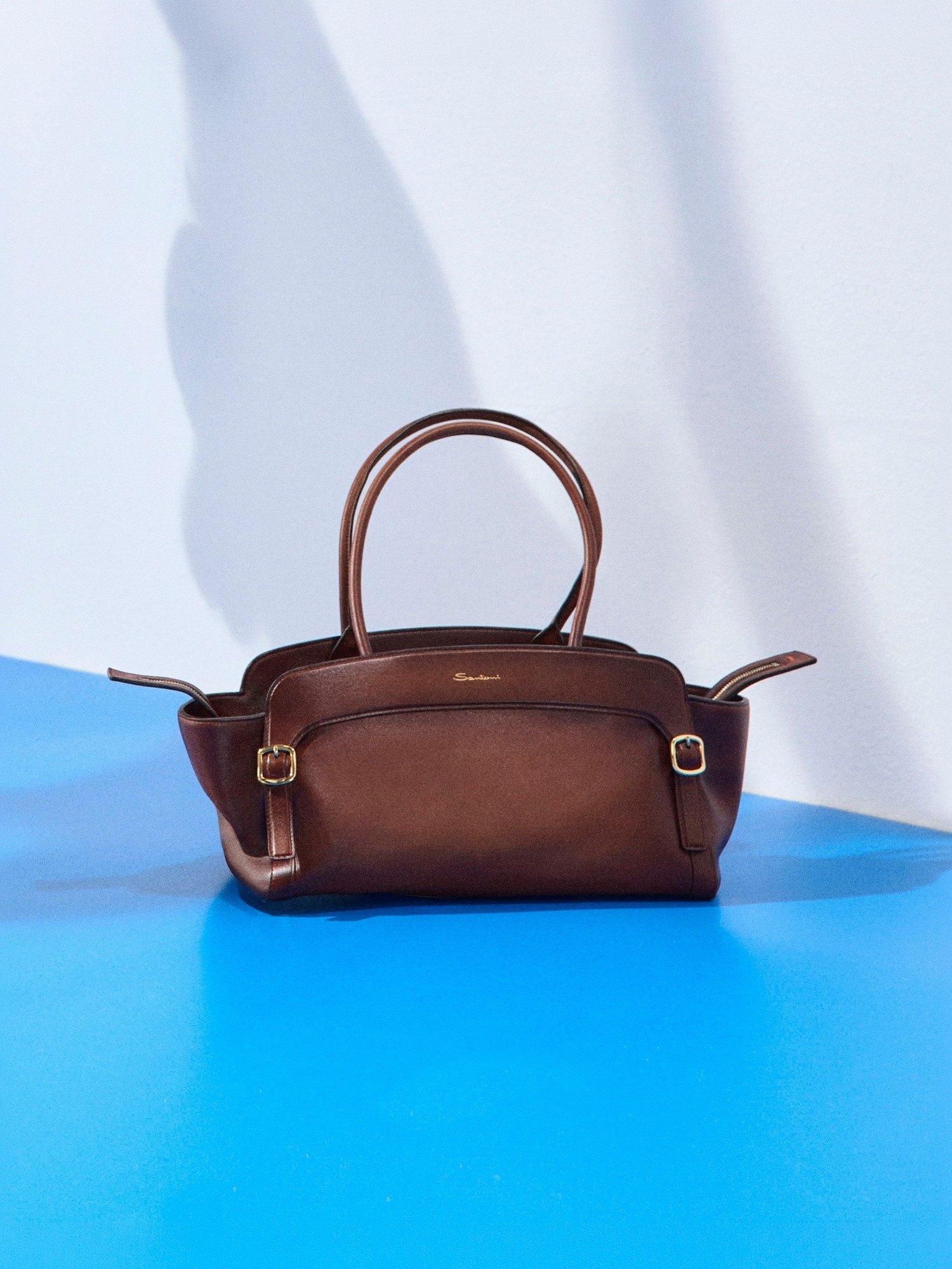 Brown leather top handle bag on a bright blue floor