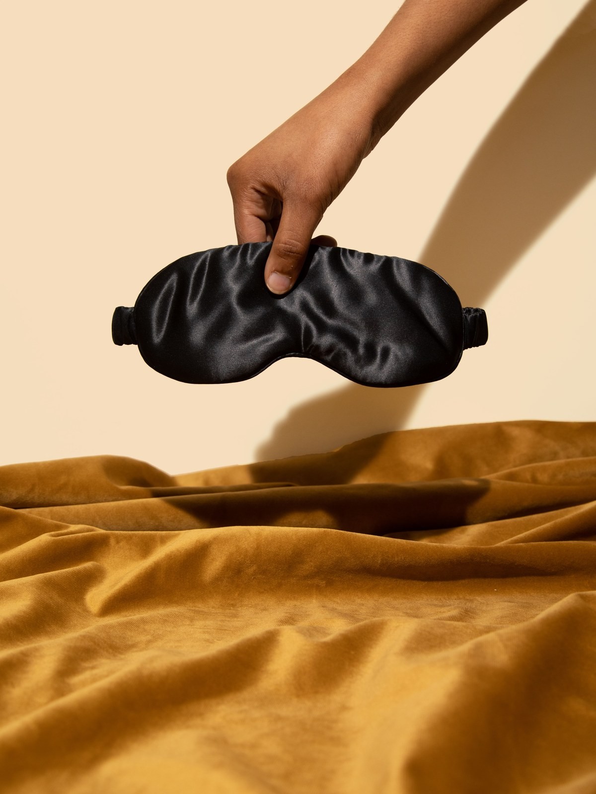 Black silk sleep mask floating above a mustard colored velvet blanket