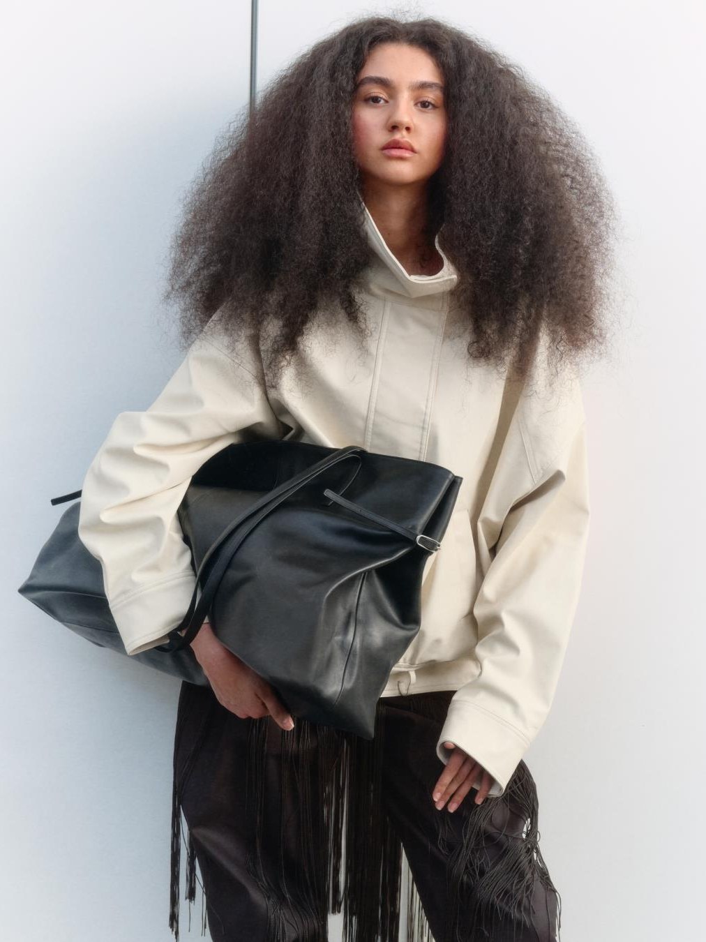 Model in a pale jacket holding a black Vagabond bag