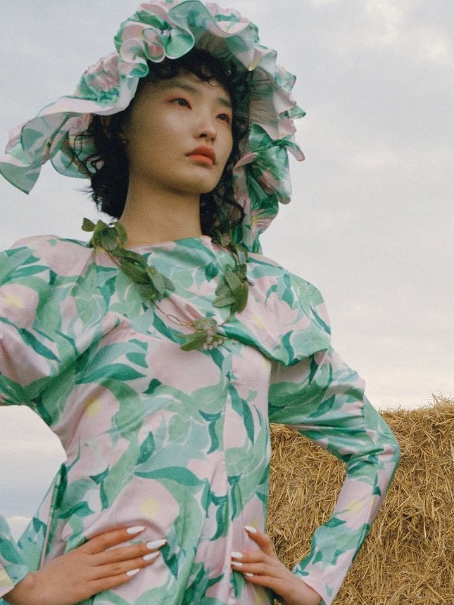 Model in a floral green and pink look beside a hay bale