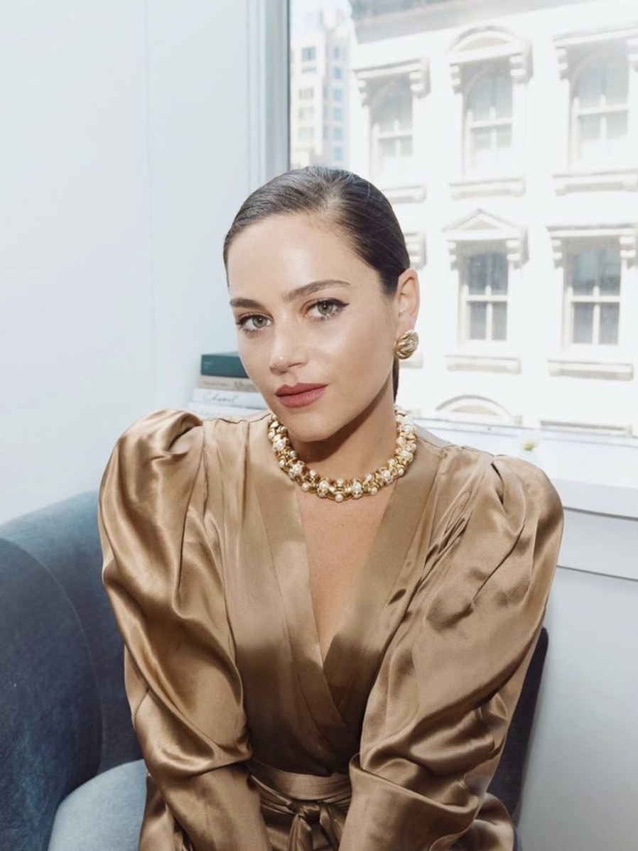 Designer Kimberly Taylor Gindi seated near a city window in a satin dress