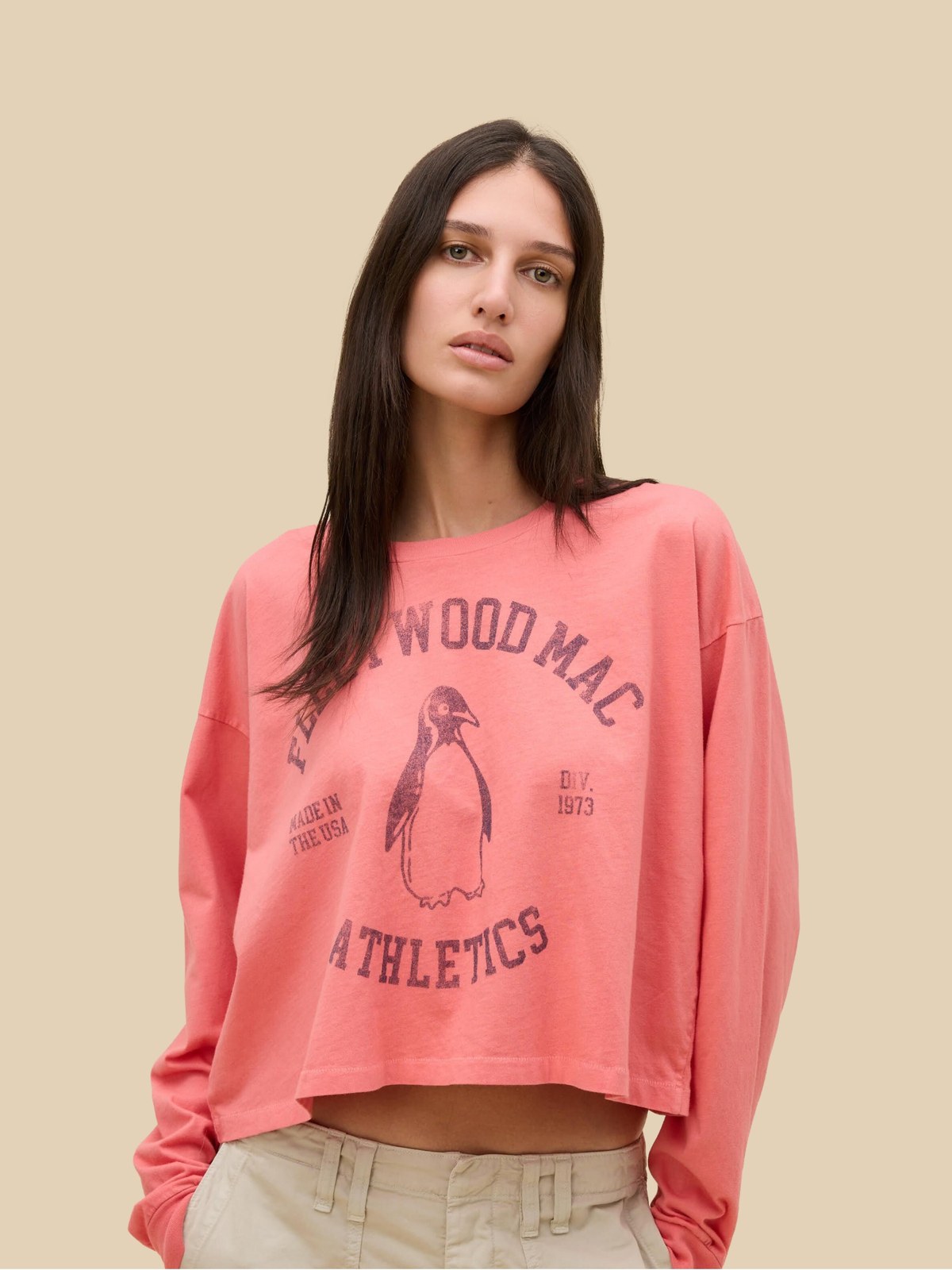 Model in a pink cropped graphic sweatshirt against a warm studio backdrop