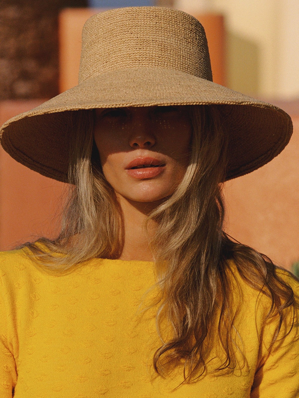 Model in a straw sun hat and yellow top against a warm backdrop